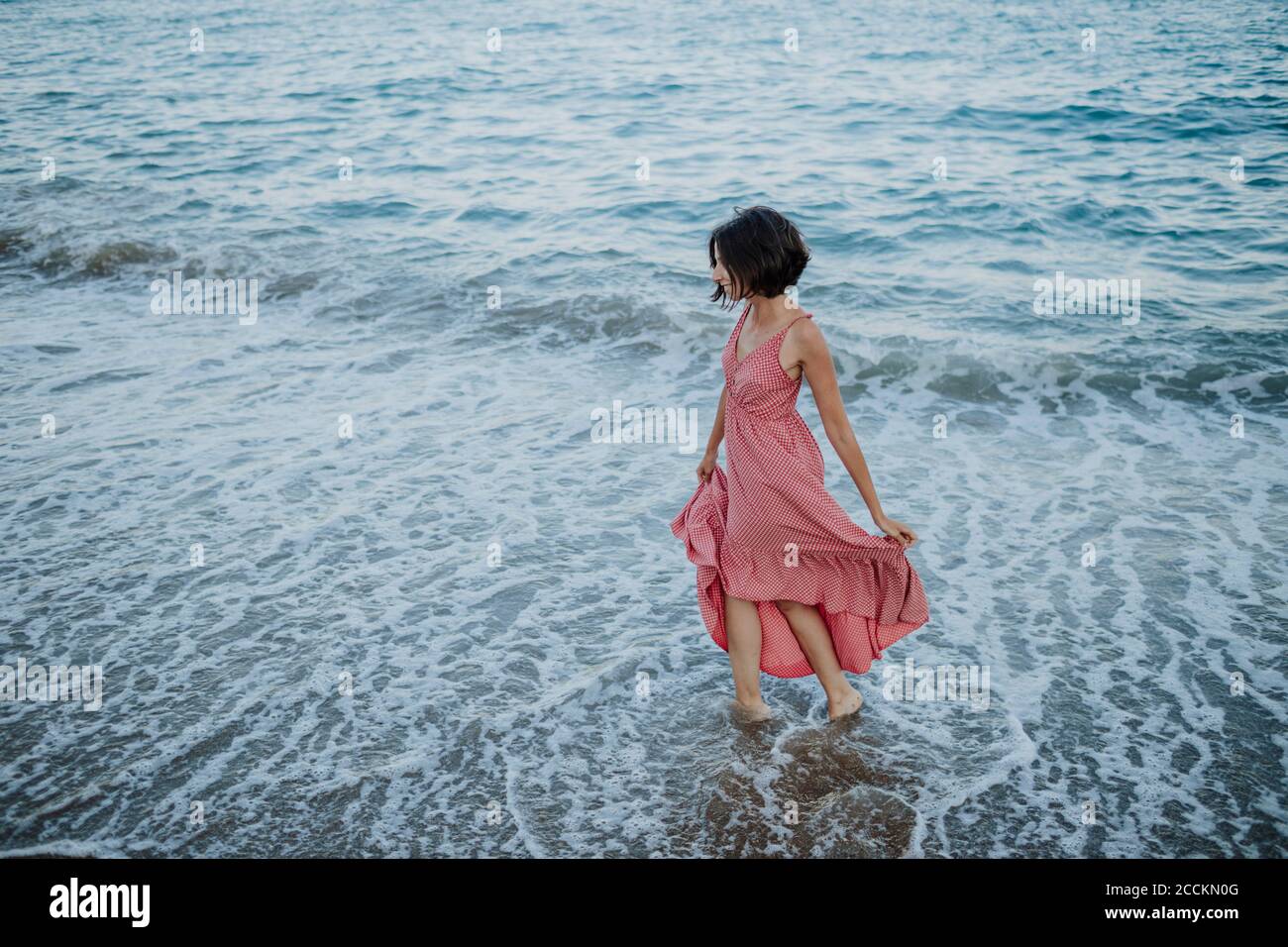 Donna mid adult che indossa un abito in piedi in mare durante il tramonto Foto Stock