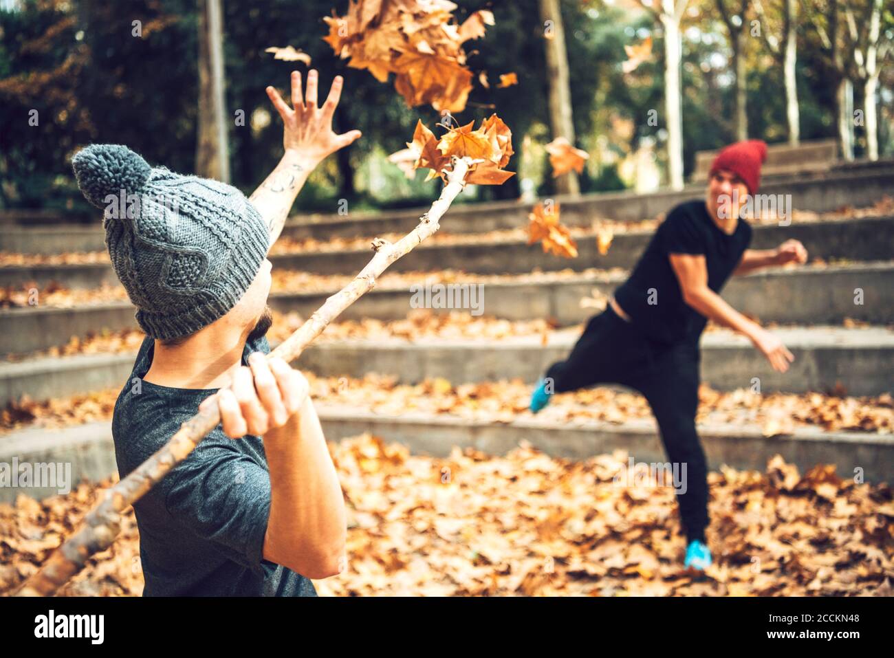 Giovani amici maschi che giocano con foglie autunnali nel parco pubblico Foto Stock