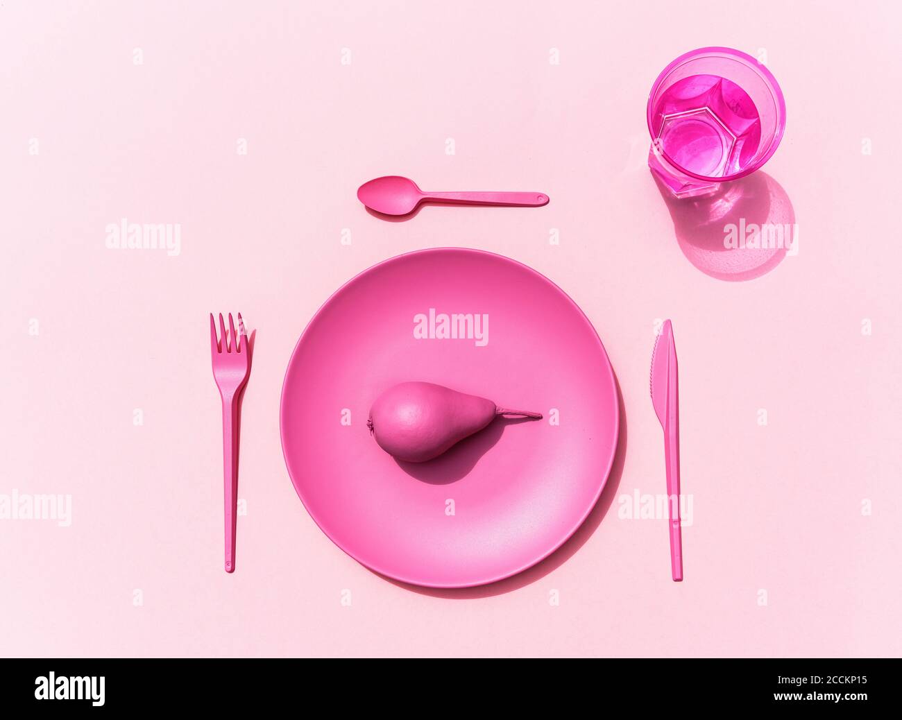 Studio di placchetta di plastica rosa, posate di plastica, bicchiere d'acqua e pera rosa Foto Stock