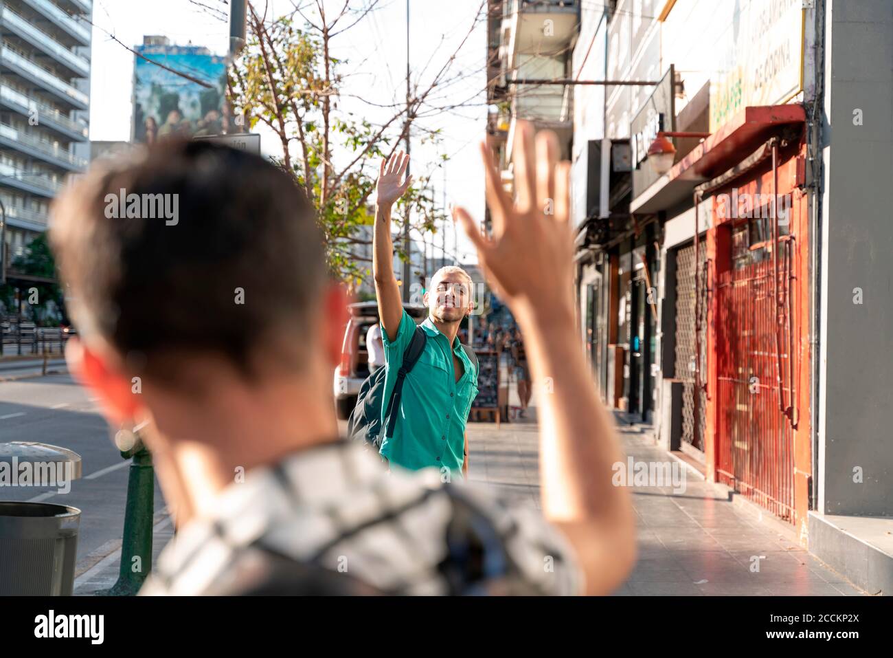 Coppia gay che si sventolano le mani l'una verso l'altra sul marciapiede dentro città Foto Stock