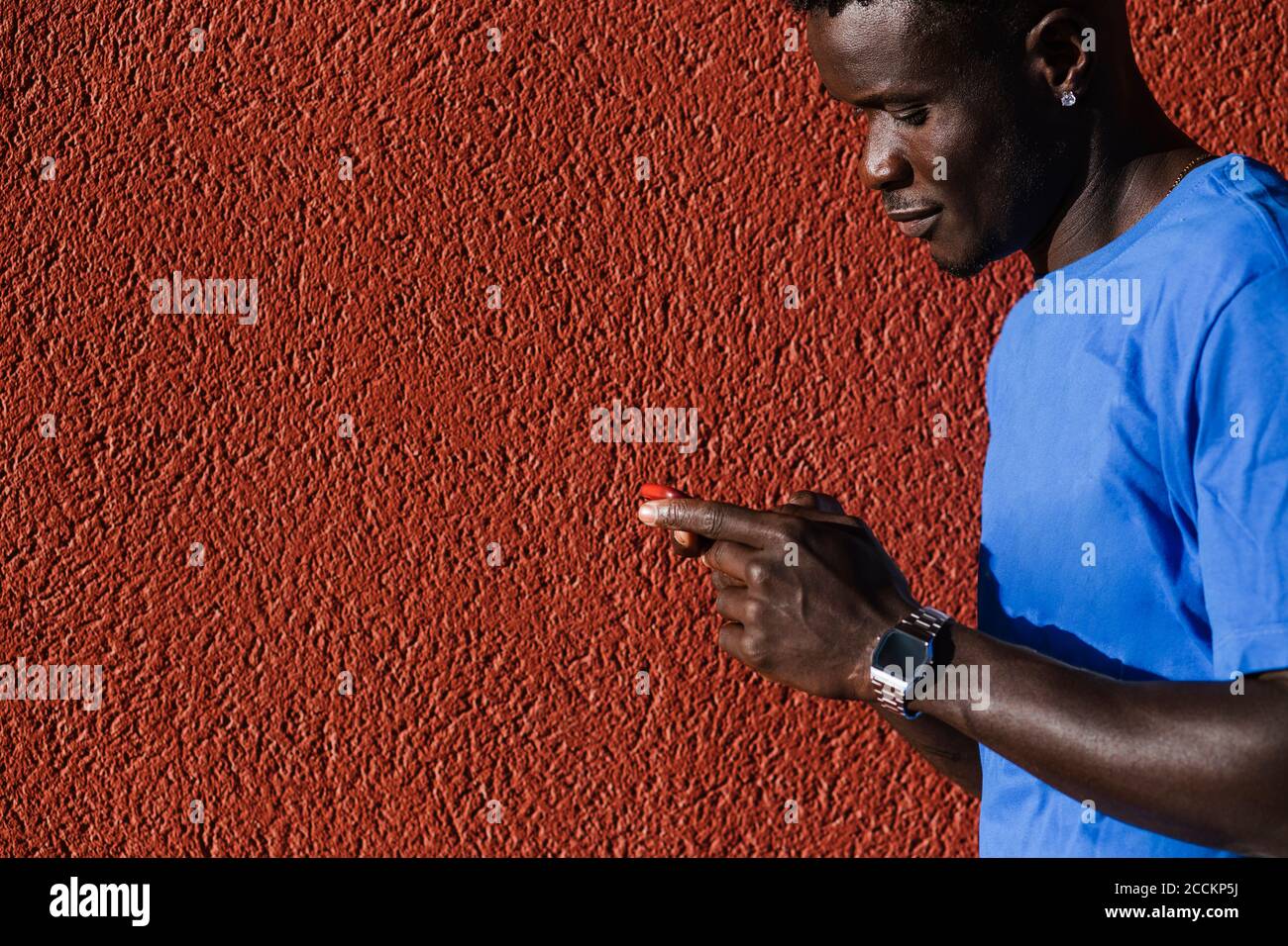 Giovane uomo che usa uno smartphone da parete rossa in città durante il giorno di sole Foto Stock