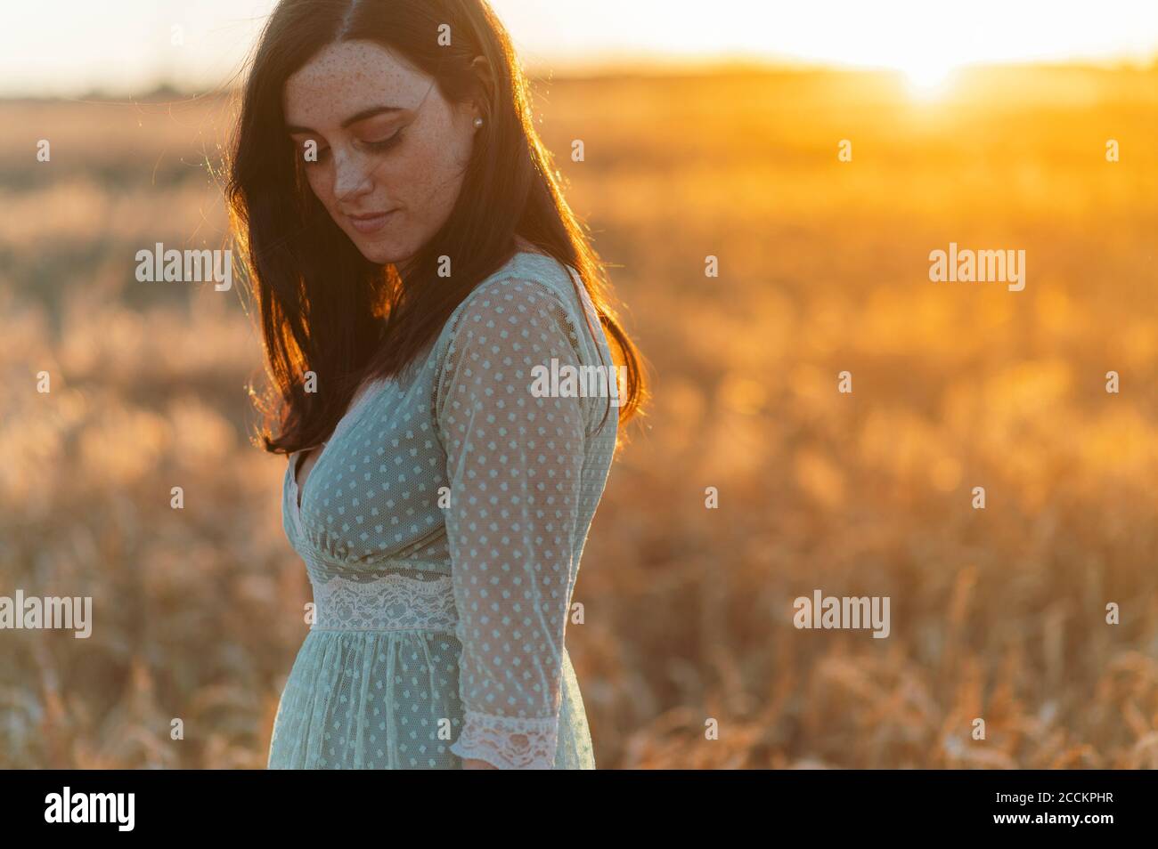 Donna giovane premurosa che guarda giù mentre si sta in fattoria a. tramonto Foto Stock