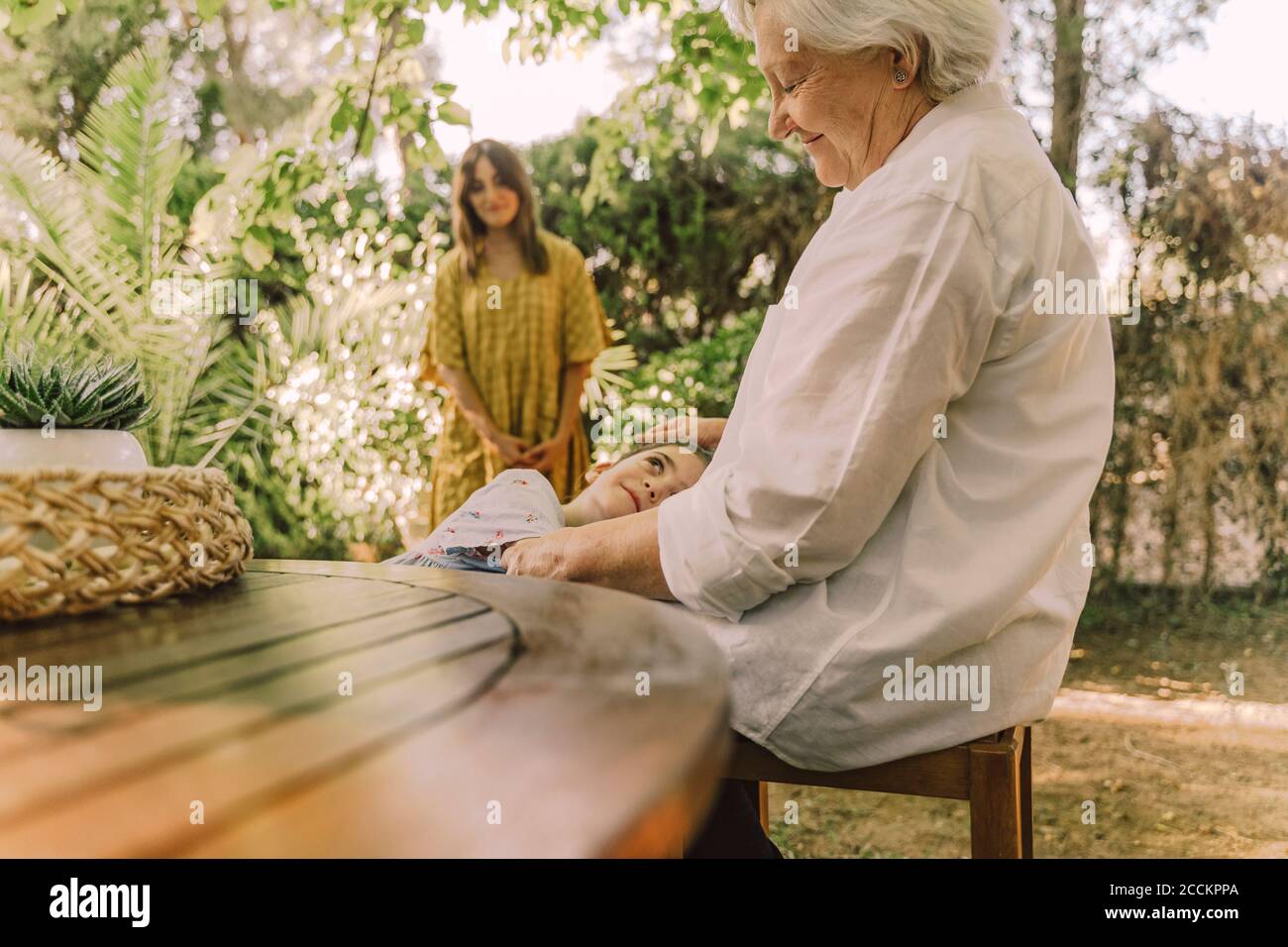 Donna che guarda la ragazza sdraiata sul grembo della nonna in cortile Foto Stock