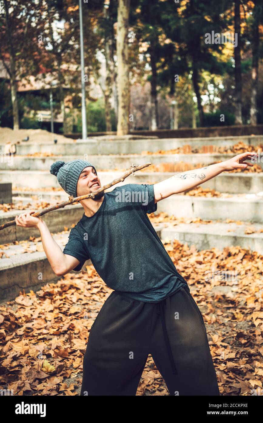 Sorridente uomo in maglia cappello gettando bastone nel parco durante autunno Foto Stock
