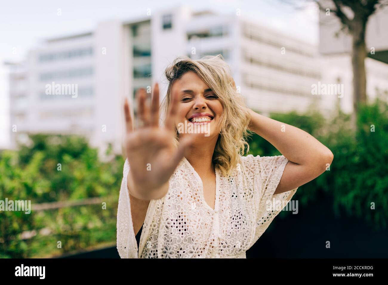 Giovane donna sorridente con la mano in capelli che mostra il gesto di stop Foto Stock