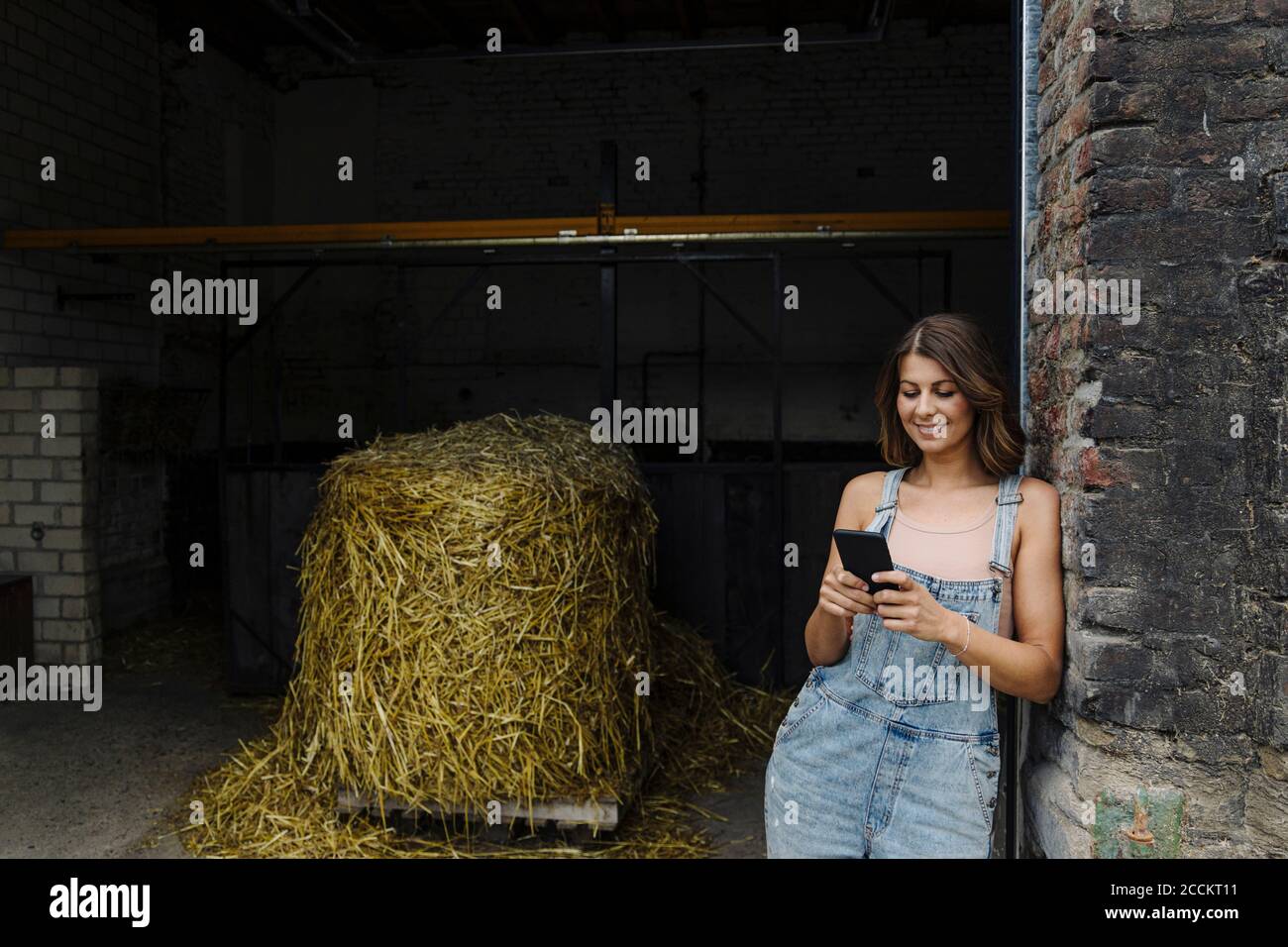 Giovane donna che usa il telefono cellulare in un fienile su un fattoria Foto Stock