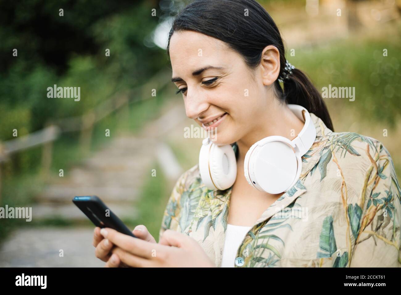 Donna sorridente mentre invia messaggi di testo dal suo smartphone Foto Stock