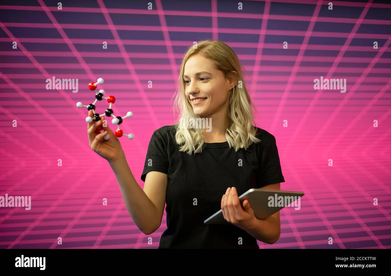 Donna scienziata che tiene in piedi un modello molecolare e un tablet digitale rispetto al modello a griglia Foto Stock