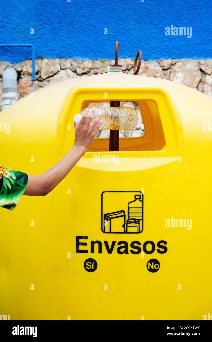 Primo piano di una donna che mette una bottiglia di plastica nel contenitore di riciclaggio Foto Stock