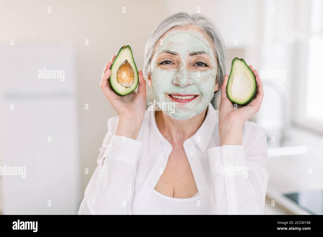 Concetto di bellezza, antirughe e dermocosmesi. Primo piano di felice bella donna capelli grigi senior in camicia bianca, con maschera facciale in argilla di fango, mostra Foto Stock