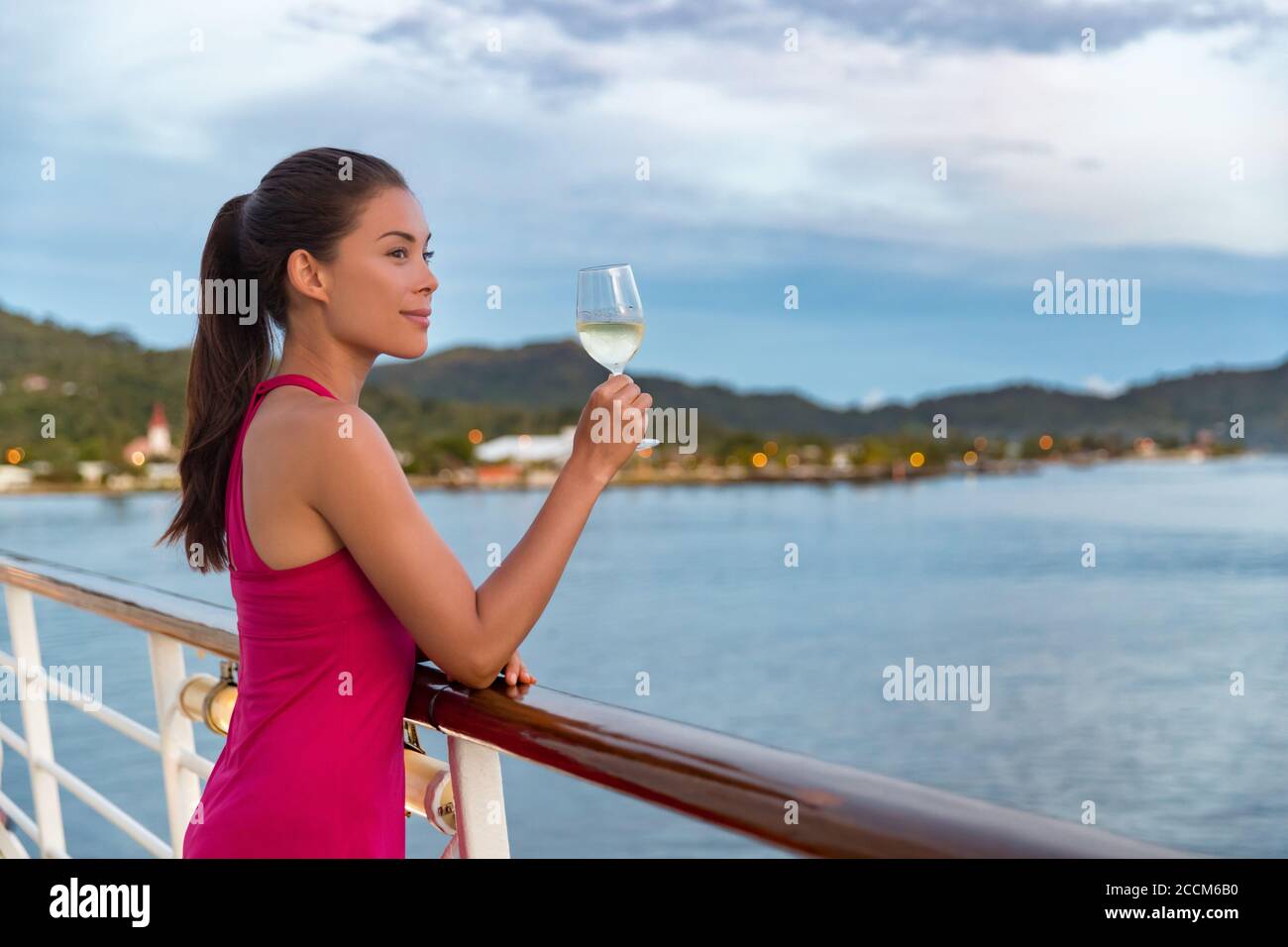 Lussuosa nave da crociera vacanza elegante donna bere un bicchiere di champagne a cena godendo di vista oceano dalla barca. Signora asiatica in abito rosso rilassante Foto Stock