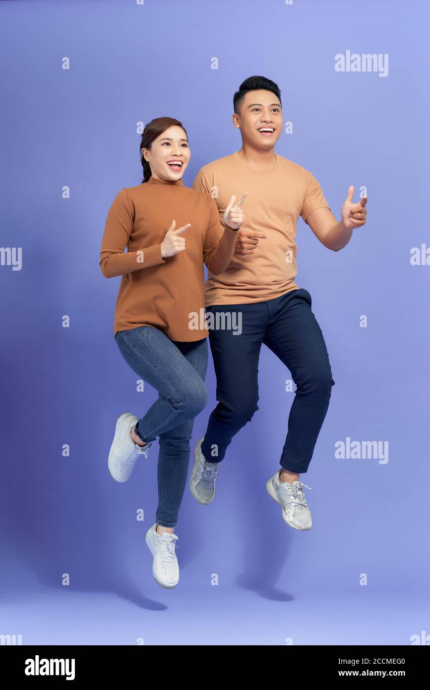Eccitato giovane coppia asiatica uomo e donna saltando e puntando con felice e divertente su sfondo viola Foto Stock