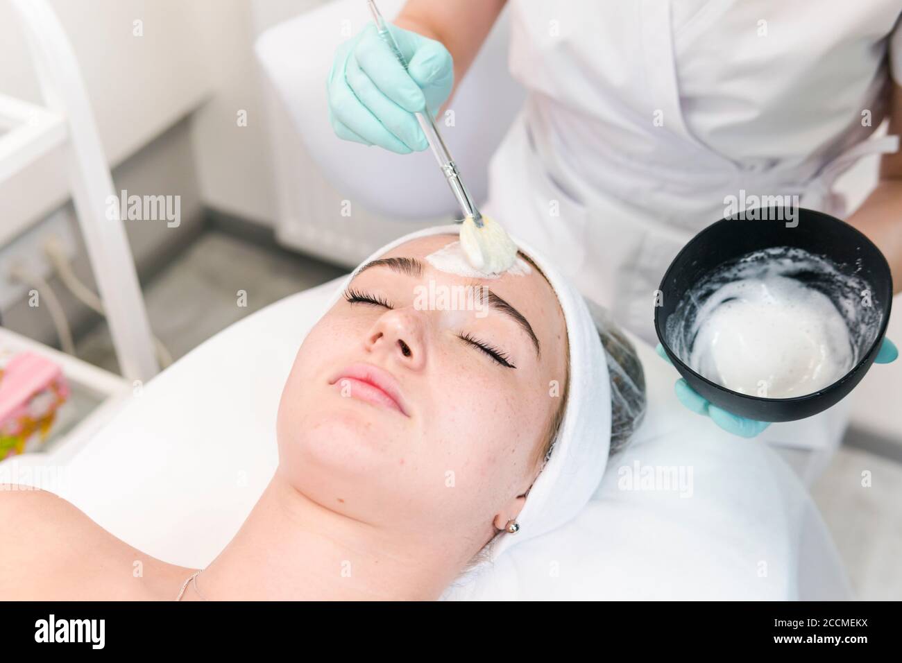 La giovane cliente femminile del salone cosmetico che ha una maschera facciale di pulizia. La procedura di applicazione di una maschera di peeling al viso. Concetti di cura della pelle Foto Stock