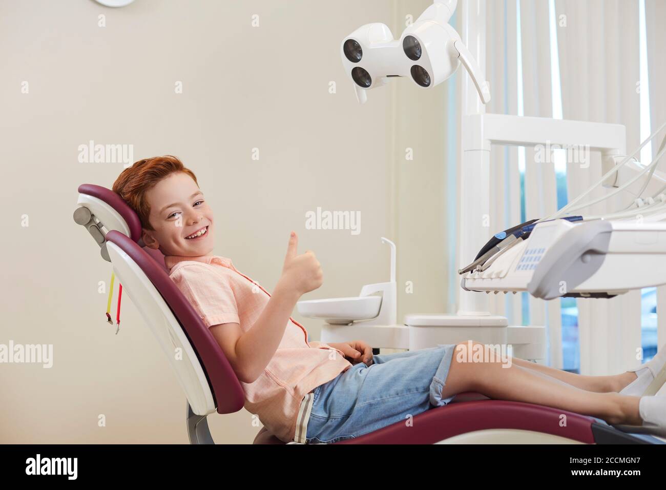 Clinica dentale. Ragazzo sorridente che mostra i pollici in su segno e guardando la macchina fotografica durante la visita del dentista Foto Stock