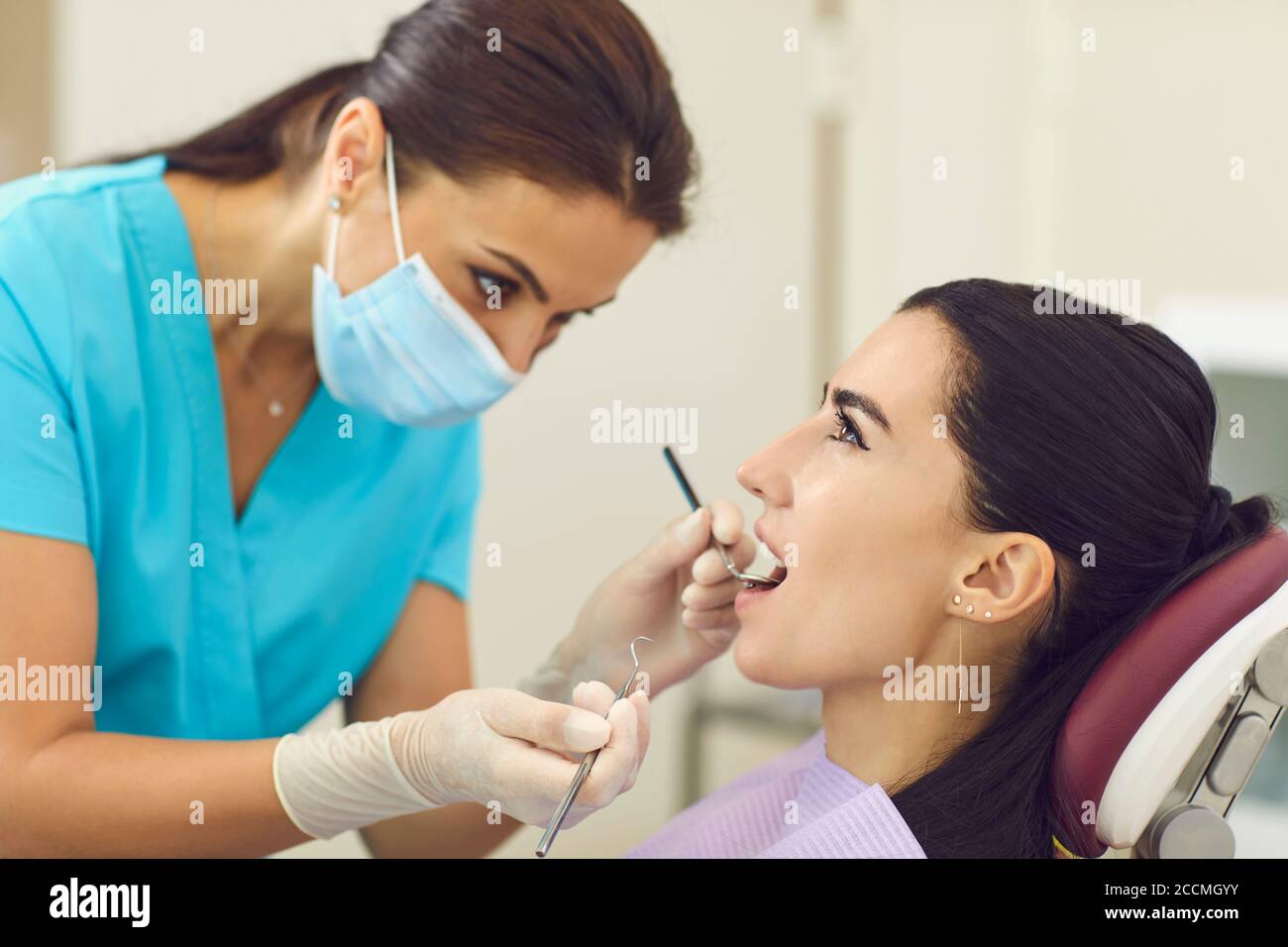 Dentista che esamina i denti dei pazienti con specchio in clinica, vista laterale Foto Stock