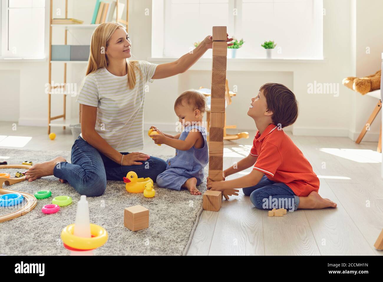 Mamma e figli stanno costruendo una torre di cubetti di legno nella stanza. La madre insegna ai bambini la giornata fuori a casa. Foto Stock