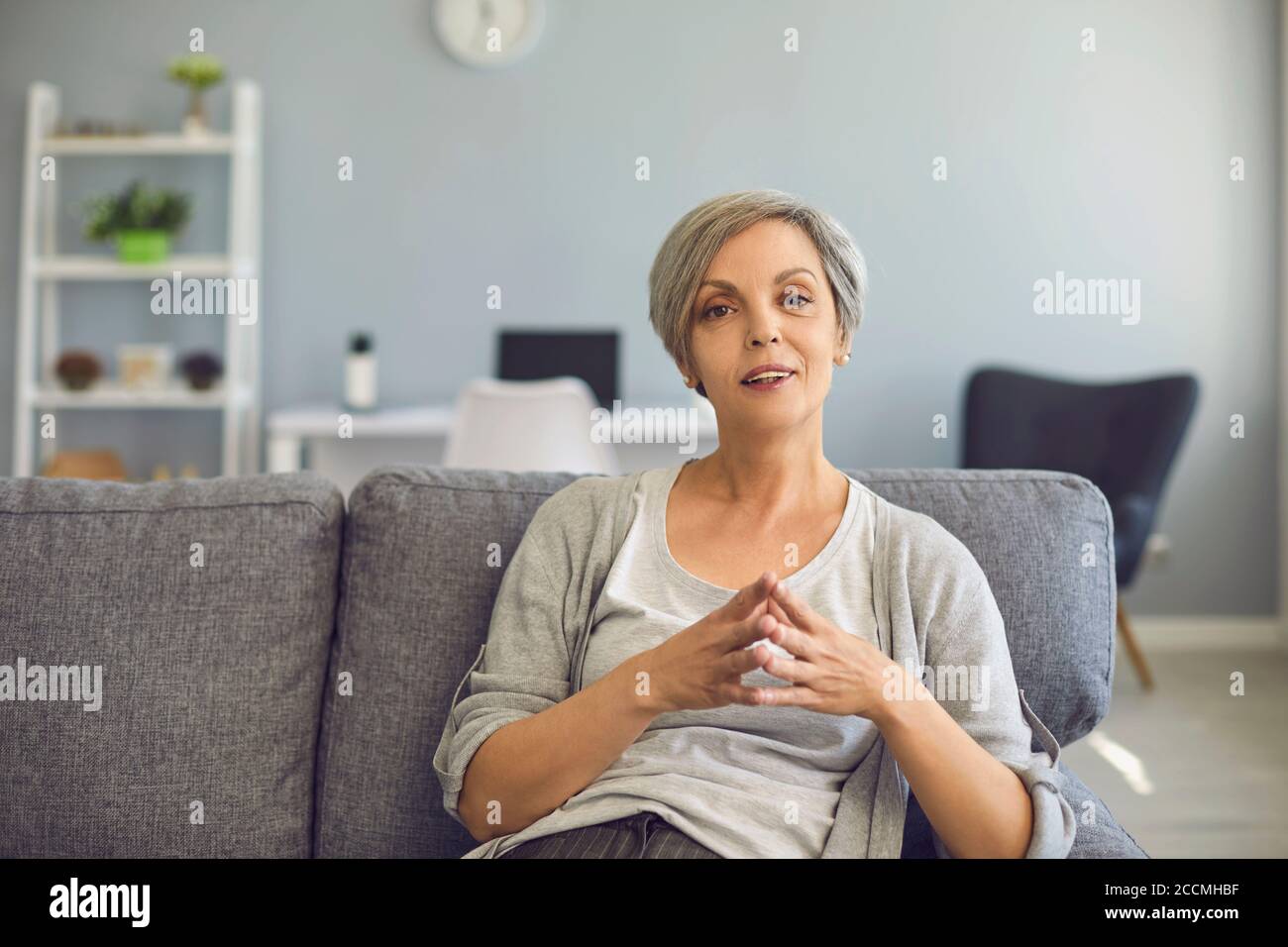 Una donna anziana guarda la telecamera ascoltando attentamente una registrazione video di una conferenza online a casa. Foto Stock
