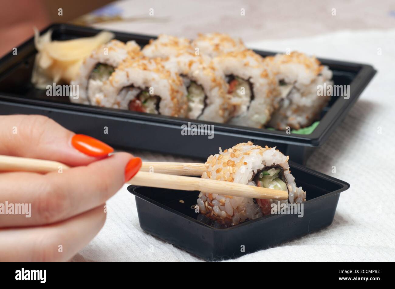 Donna che mangia il sushi consegnato a casa da un contenitore con bastoncini giapponesi. Messa a fuoco selettiva. Foto Stock