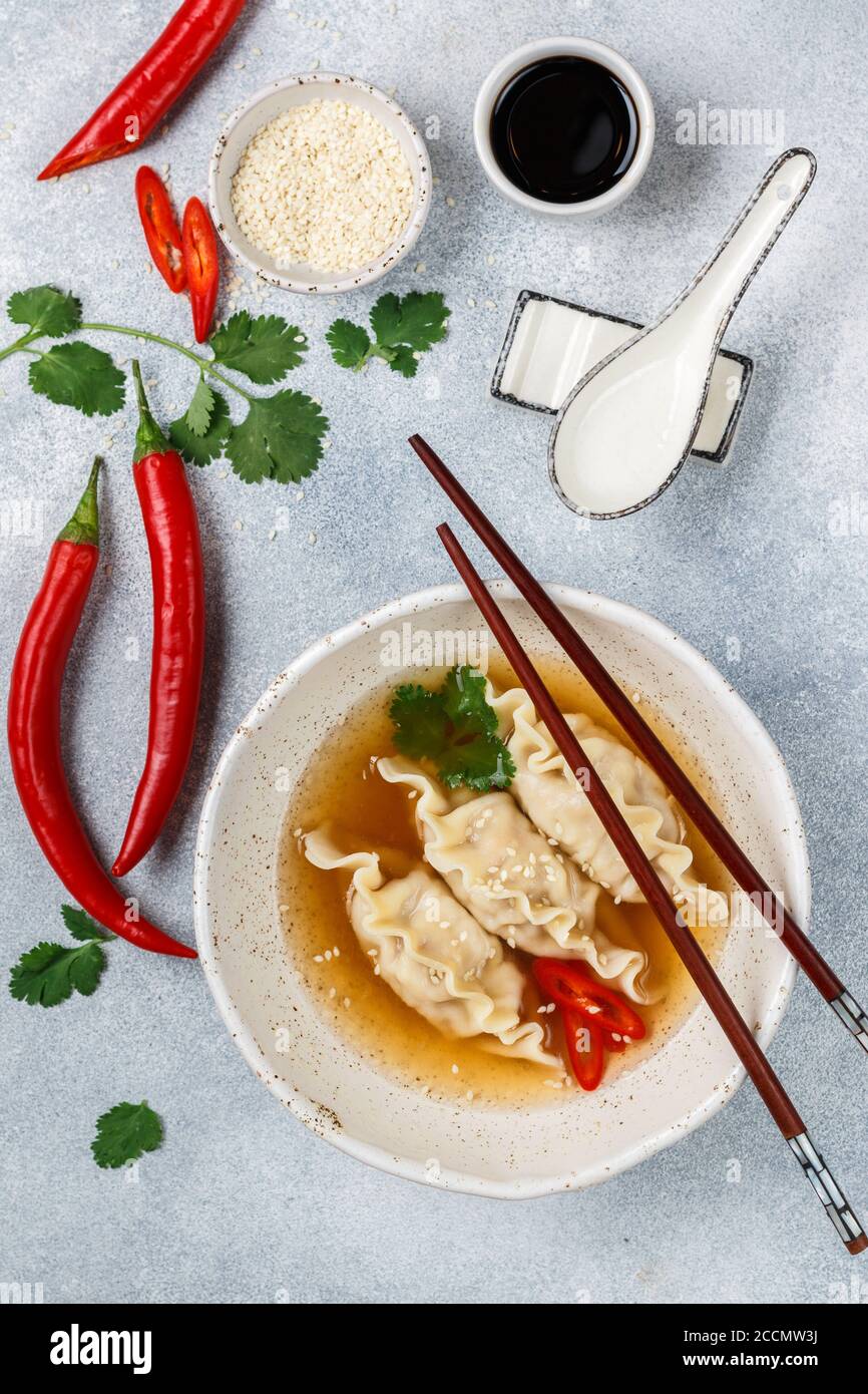 Zuppa calda fresca con gnocchi (gedza, wontons) di pollo, maiale o gamberetti con salsa di soia, peperoncino, coriandolo e semi di sesamo in un piatto bianco Foto Stock