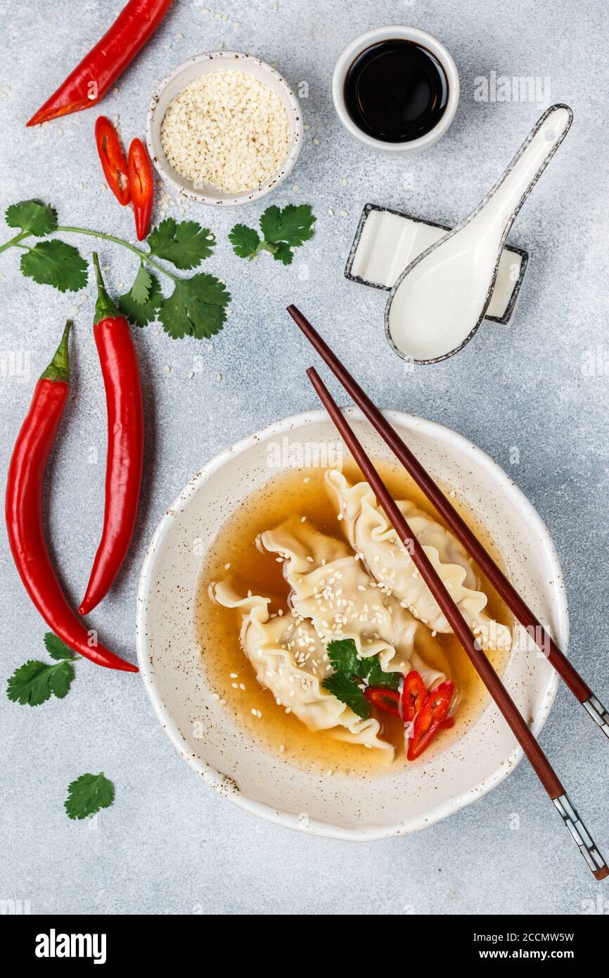 Zuppa calda fresca con gnocchi (gedza, wontons) di pollo, maiale o gamberetti con salsa di soia, peperoncino, coriandolo e semi di sesamo in un piatto bianco Foto Stock