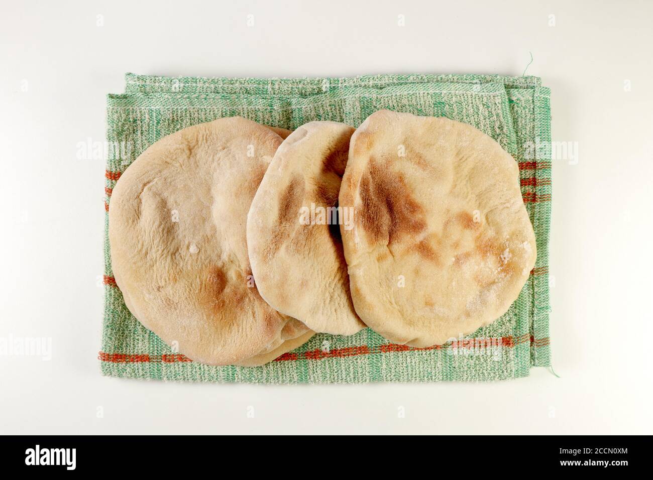 pita appena sfornata o pane arabico su un panno rustico e una tavola di legno su una superficie bianca Foto Stock