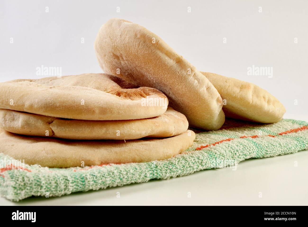 pita appena sfornata o pane arabico su un panno rustico e una tavola di legno su una superficie bianca Foto Stock