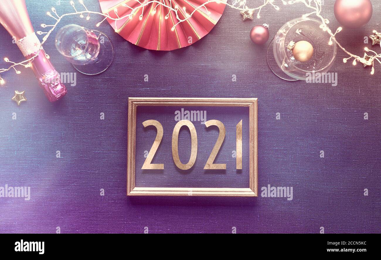Set da tavolo New Year 2021 con piatto bianco, utensili dorati, tovagliolo rosso scuro e decorazioni dorate. Disposizione piatta, vista dall'alto su bac in tessuto di lino blu scuro Foto Stock
