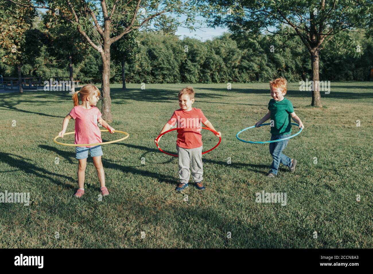 Carino sorridente caucasico prescolare ragazza ragazzi amici giocare con hoola in parco esterno. Attività sportive per bambini. Stile di vita felice infanzia. Estate Foto Stock