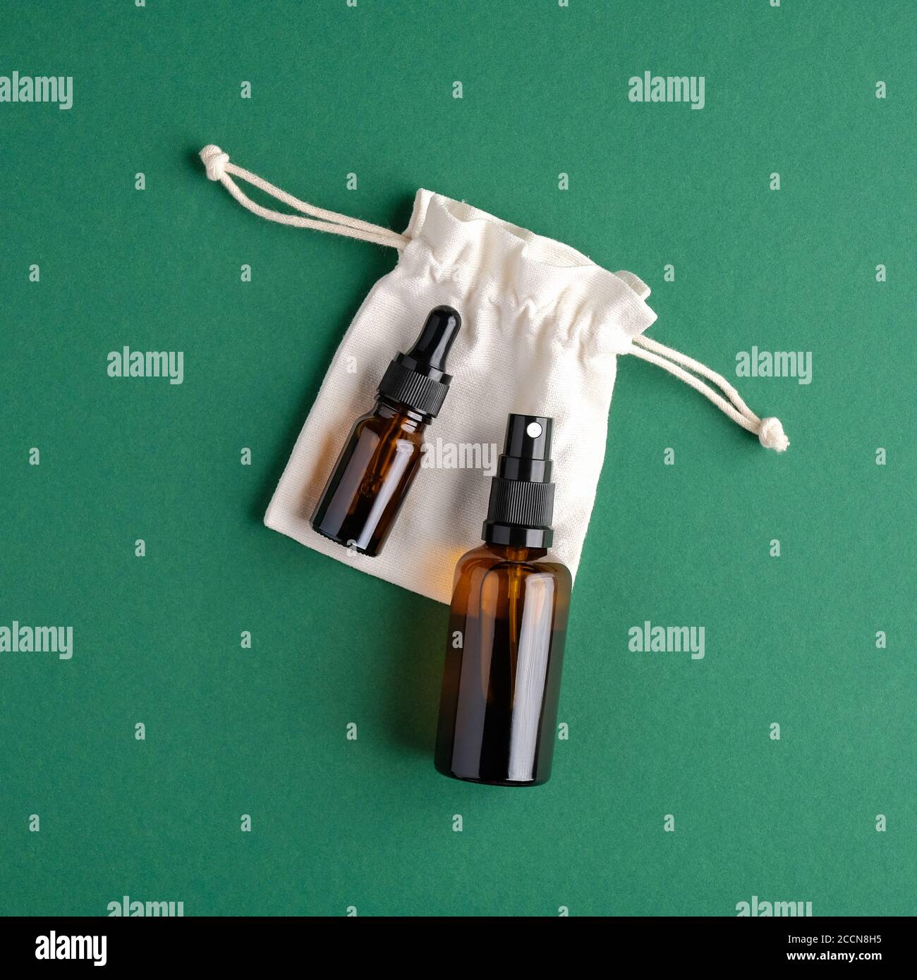 Bottiglie cosmetiche in vetro ambrato e sacchetto su sfondo verde. Nessun spreco, design di confezionamento di prodotti di bellezza ecocompatibili. Disposizione piatta, vista dall'alto. Foto Stock