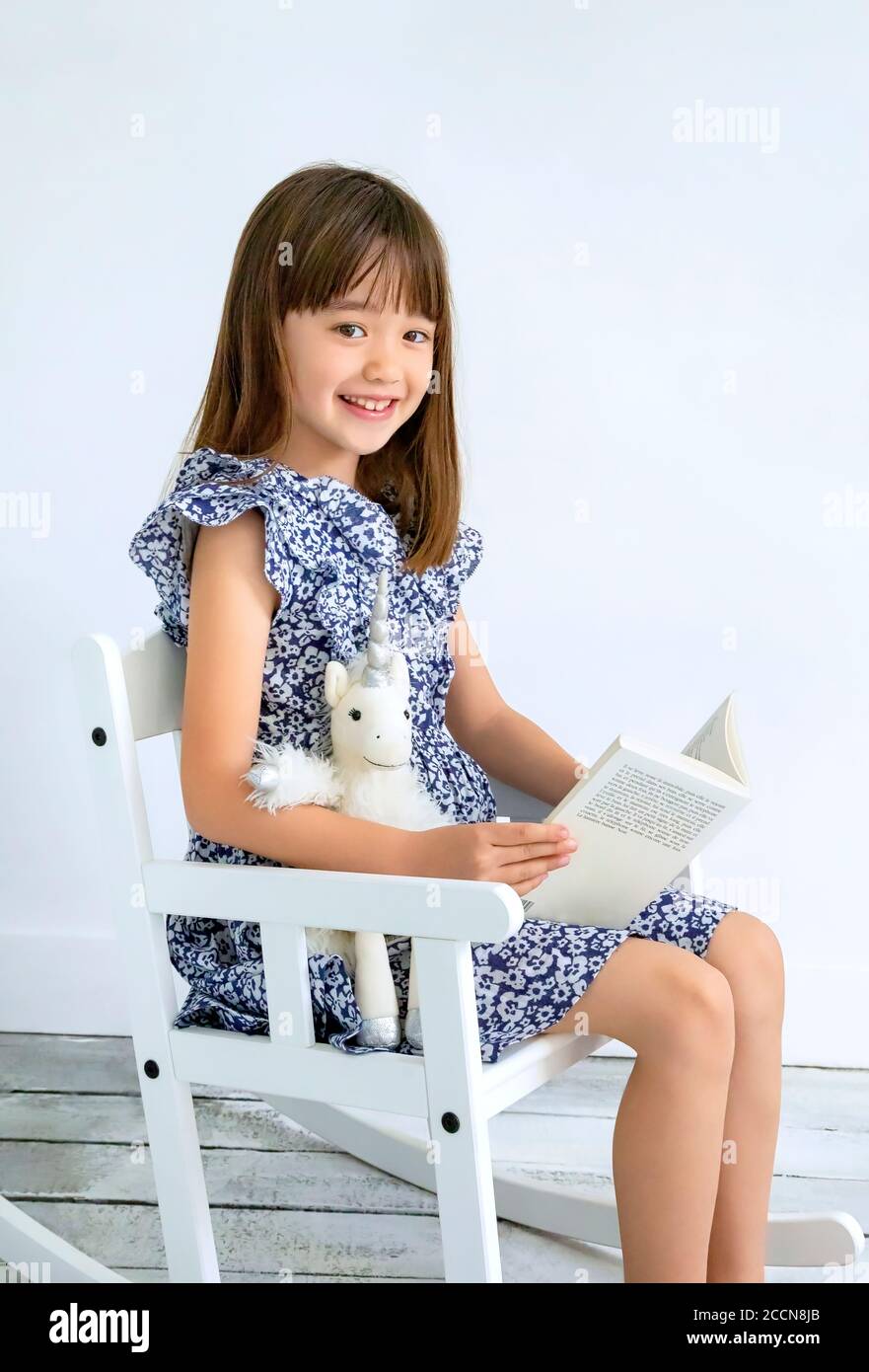 Ragazza di sette anni che legge un libro su un dondolo sedia Foto Stock