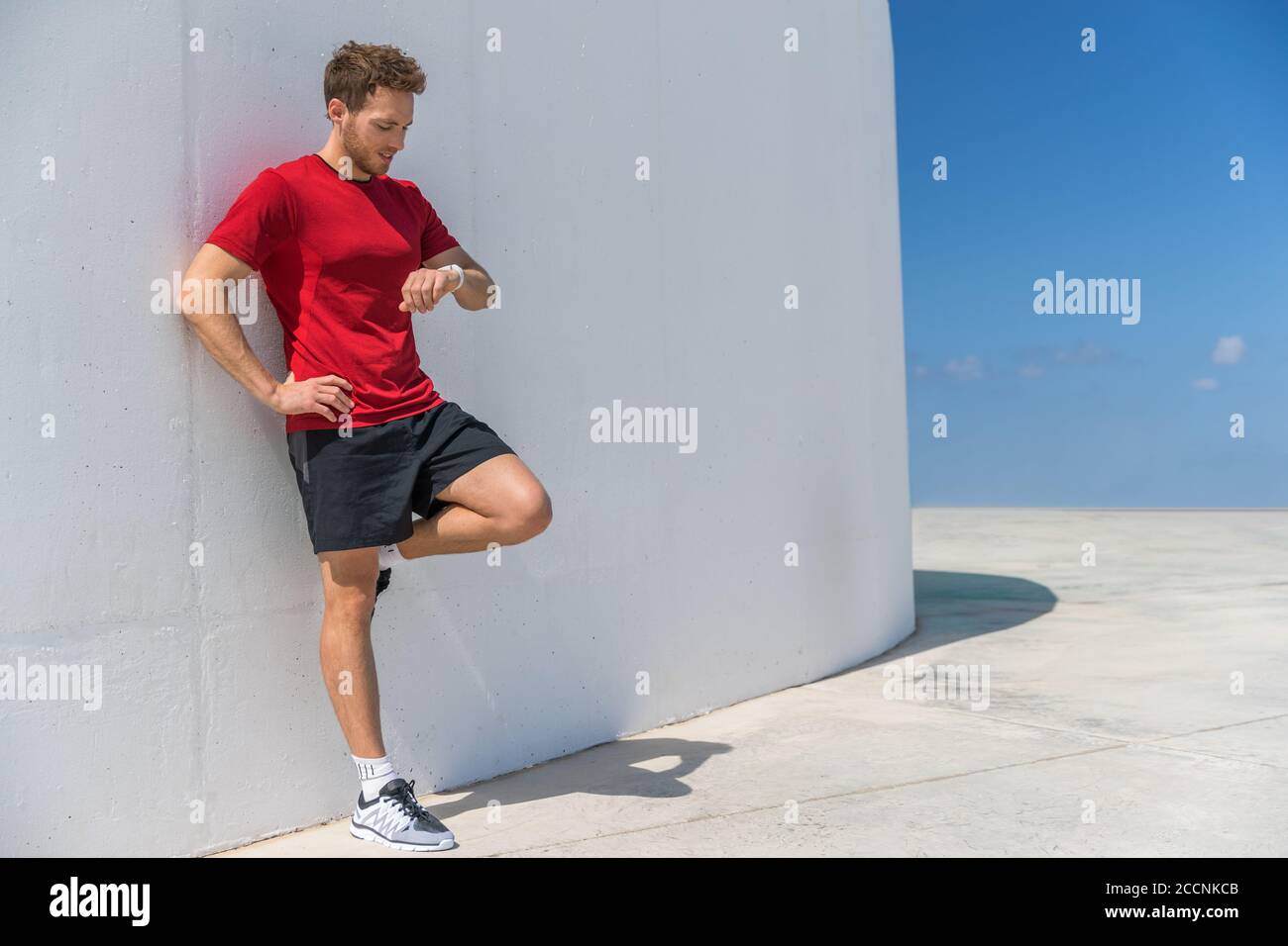 Il runner man di smartwatch controlla i progressi dell'orologio sportivo Smart fitness durante l'allenamento cardiofitness break. Un atleta che si rilassa utilizzando l'app online Foto Stock