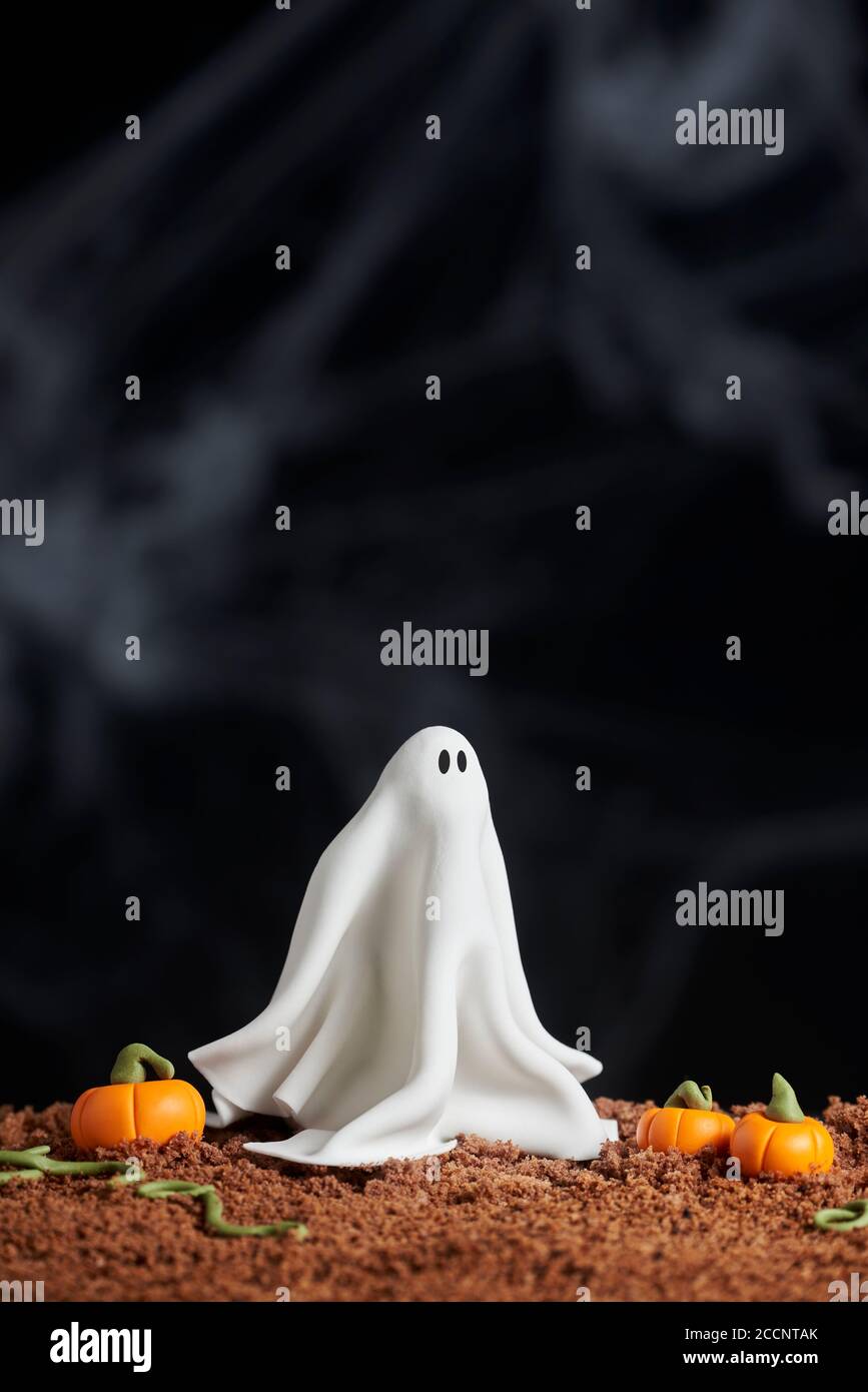 Scena di Halloween, fantasma e zucche di pasta di zucchero su terreno torta al cioccolato, sfondo nero, spazio copia Foto Stock