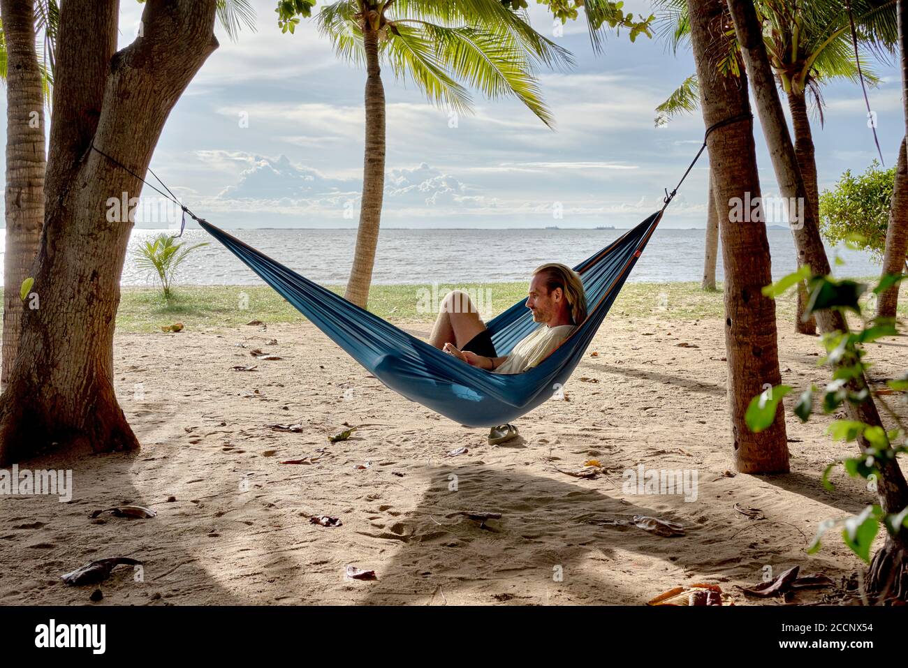 Spiaggia amaca. Uomo che si rilassa in un'amaca tra gli alberi su una spiaggia tropicale contro il sole che tramonta. Thailandia Sud-est asiatico Foto Stock