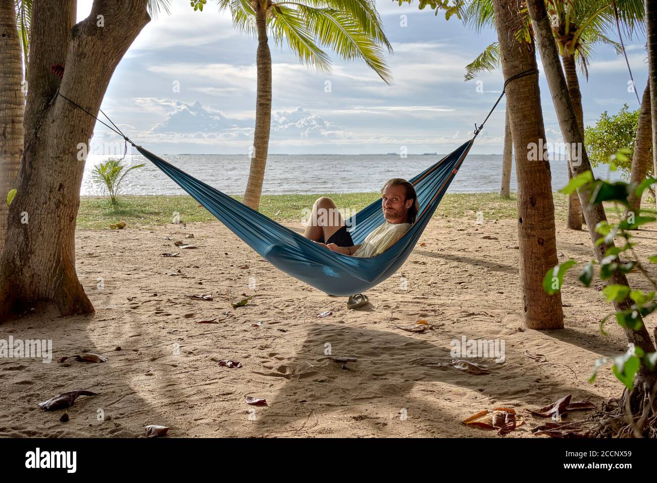Spiaggia amaca. Uomo che si rilassa in un'amaca tra gli alberi su una spiaggia tropicale contro il sole che tramonta. Thailandia Sud-est asiatico Foto Stock