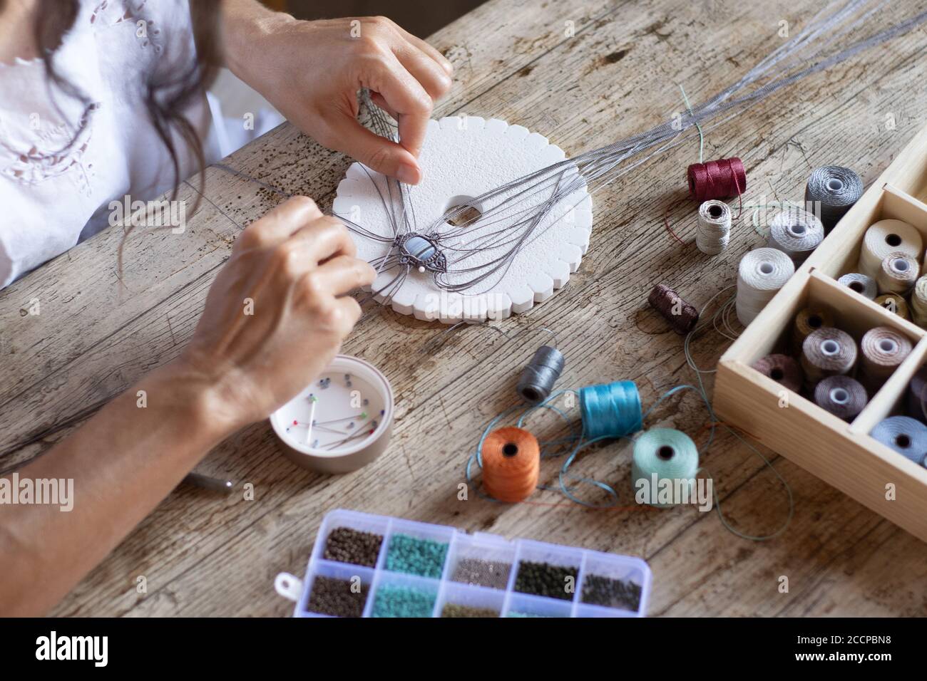 Vista ad angolo superiore di una donna che lavora da casa gioiello in micro macrame fatto a mano con spole colorate di filo - reinventate la vostra vita con lavoro indipendente Foto Stock