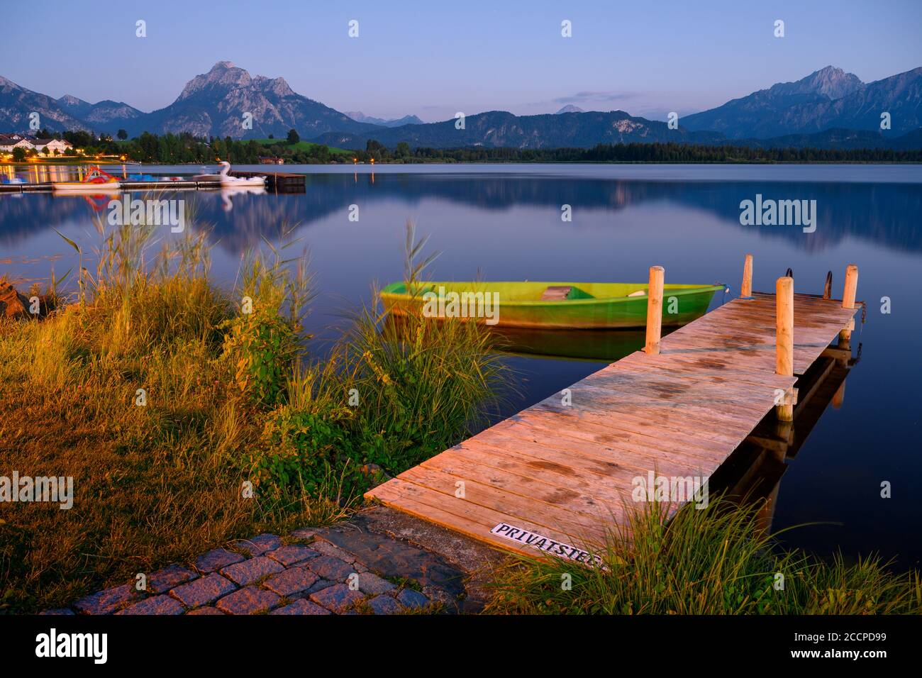 Pontile in legno a Hopfensee, sullo sfondo le Alpi e il villaggio di Hopfen am See, Baviera, Germania Foto Stock