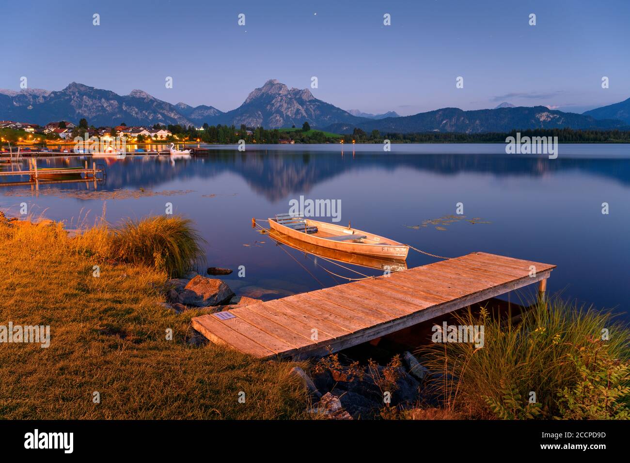 Pontile in legno a Hopfensee, sullo sfondo le Alpi e il villaggio di Hopfen am See, Baviera, Germania Foto Stock