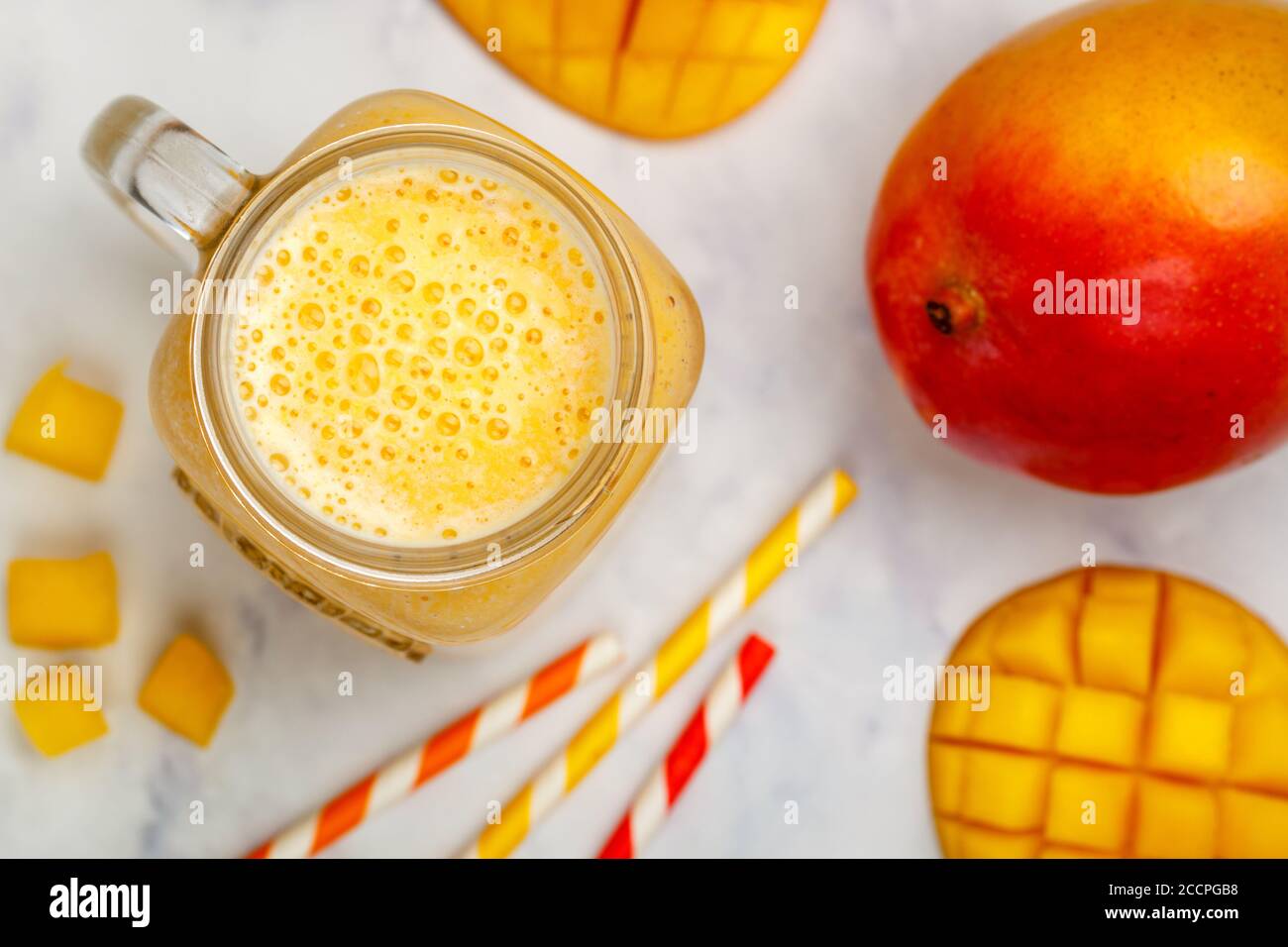 Frullato o frullato di mango fresco, yogurt o latte e cubetti di ghiaccio in vaso Mason su un tavolo di marmo. Concetto di bevande vitaminiche sane. Selectiv Foto Stock