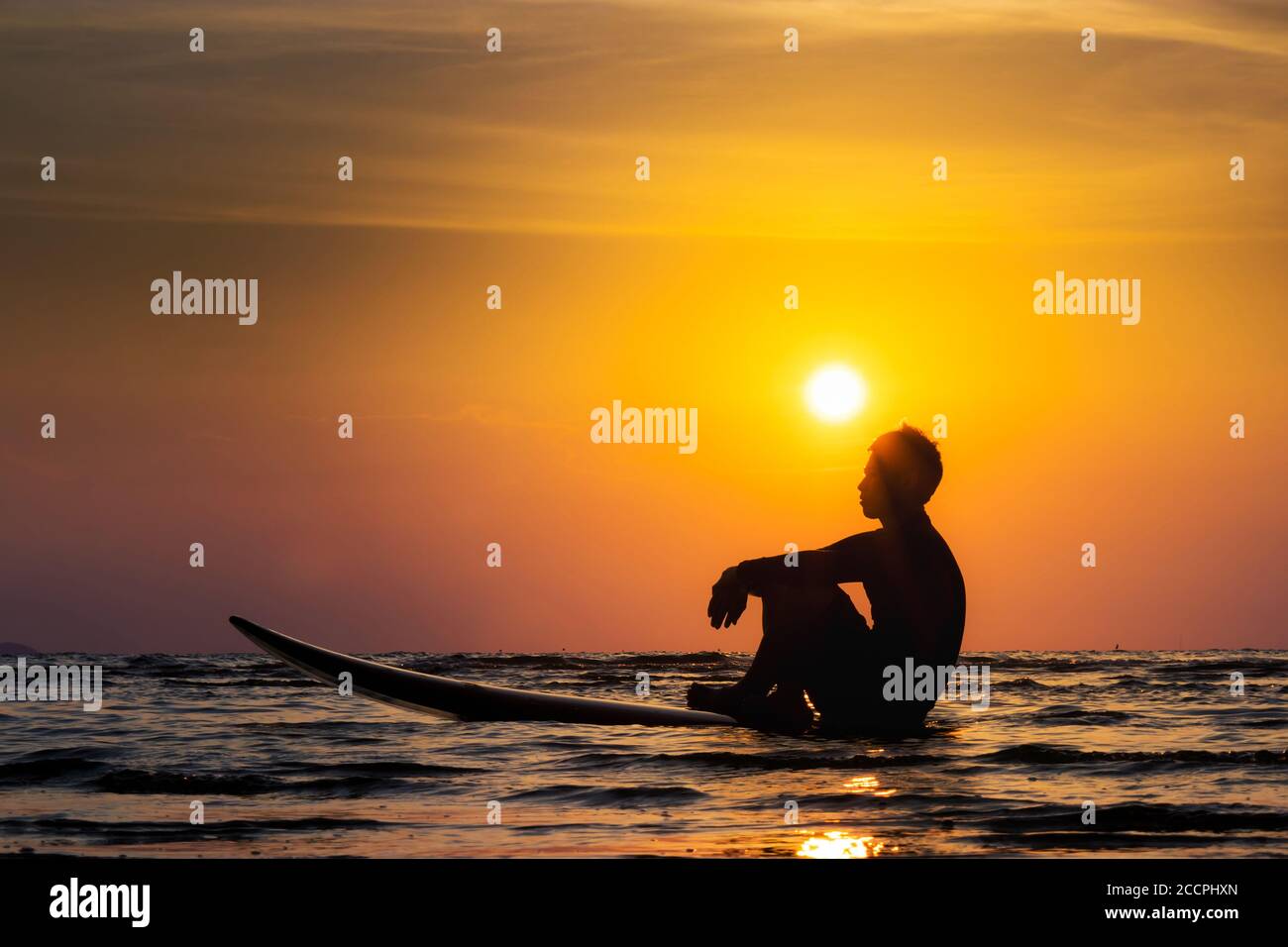 Silhouette di surf uomo sedersi su una tavola da surf. Surf alla spiaggia del tramonto. Sport acquatici all'aperto avventura lifestyle.Summer attività. Bel modello asiatico maschio Foto Stock