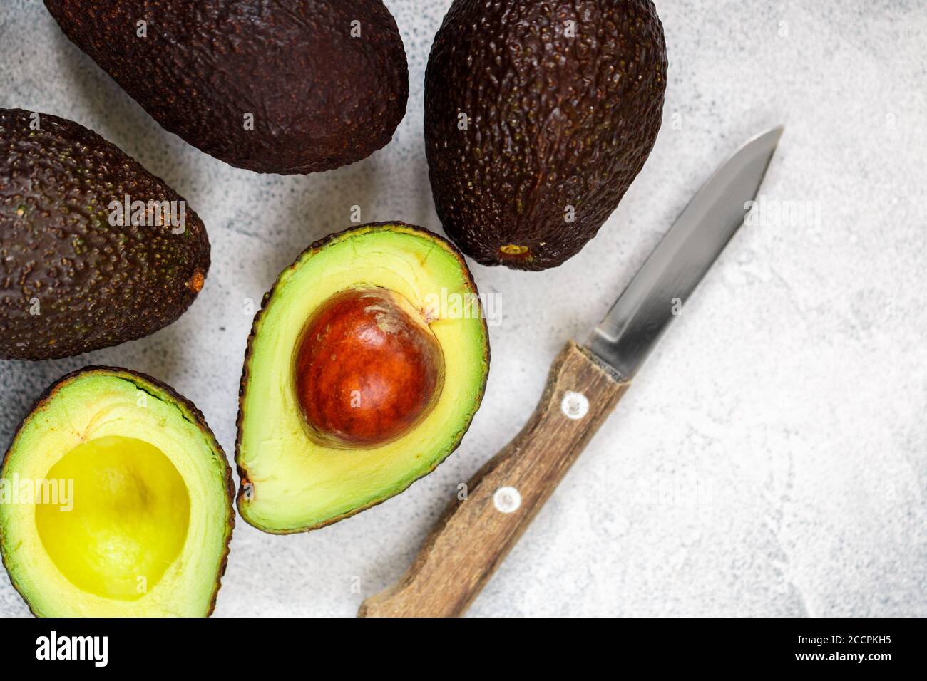 Intero e tagliato in avocado organico mezzo maturo e un coltello su sfondo grigio. Il Haas Avocado. Fonte di vitamine , oligoelementi , beta-carotene A. Foto Stock