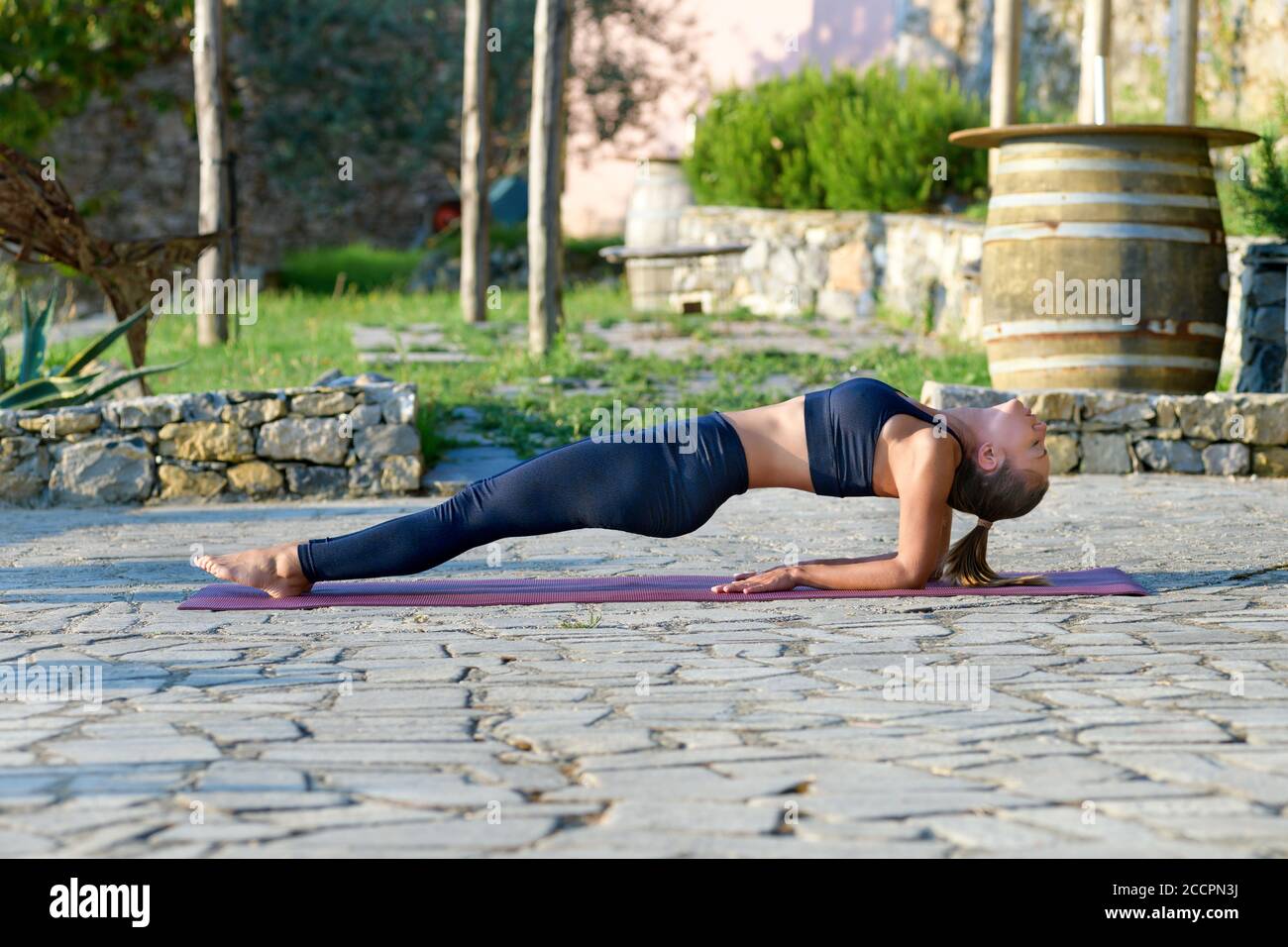 Ragazza che fa una posizione di yoga in alto in una posizione all'aperto nel giardino per rafforzare i suoi muscoli core in una salute e. concetto di fitness Foto Stock