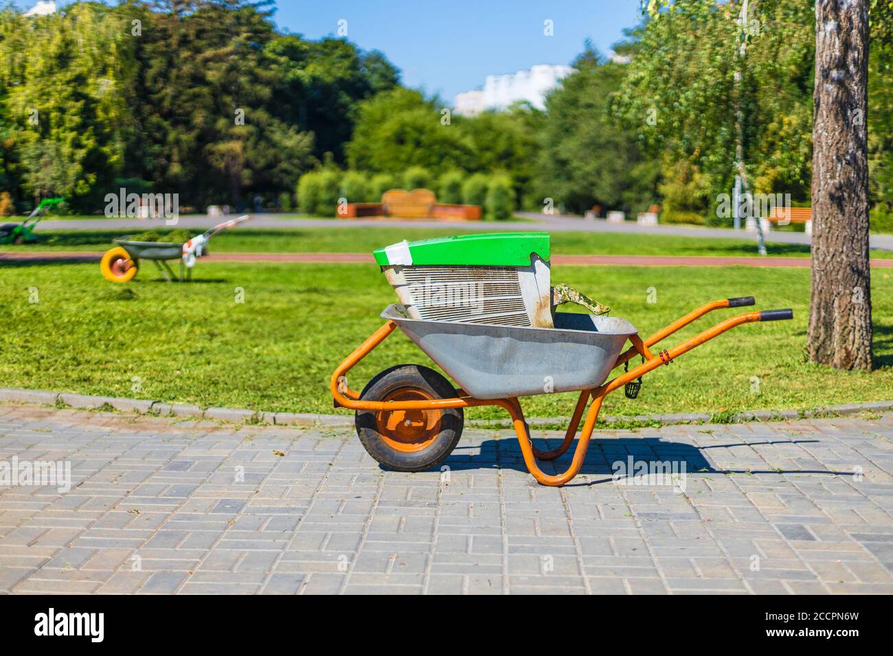 Carriola su un campo di erba verde. Carretto con carriola in metallo da giardino. Foto Stock