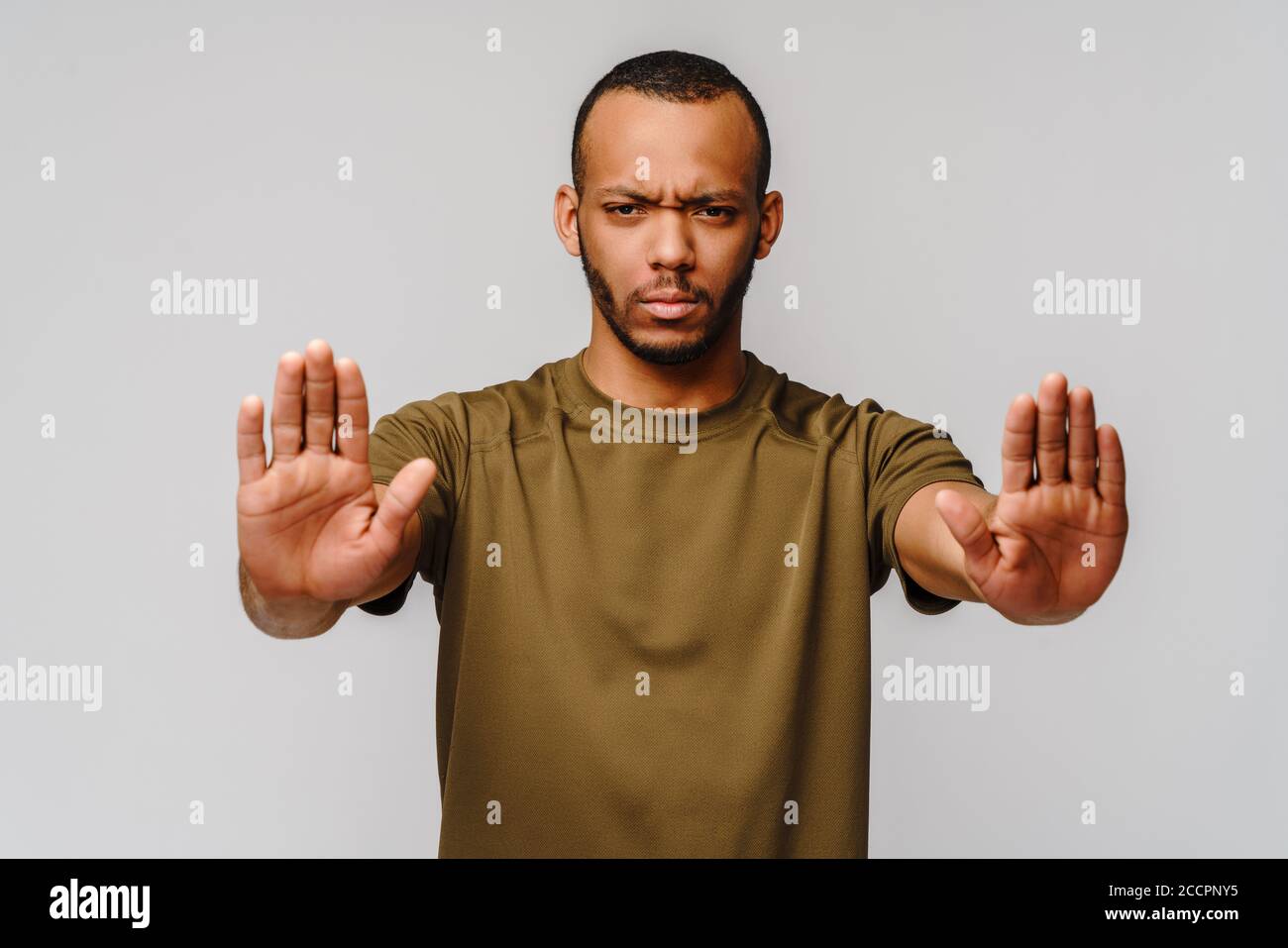 il giovane afro-americano gesturing SI FERMA con la mano sfondo grigio chiaro Foto Stock