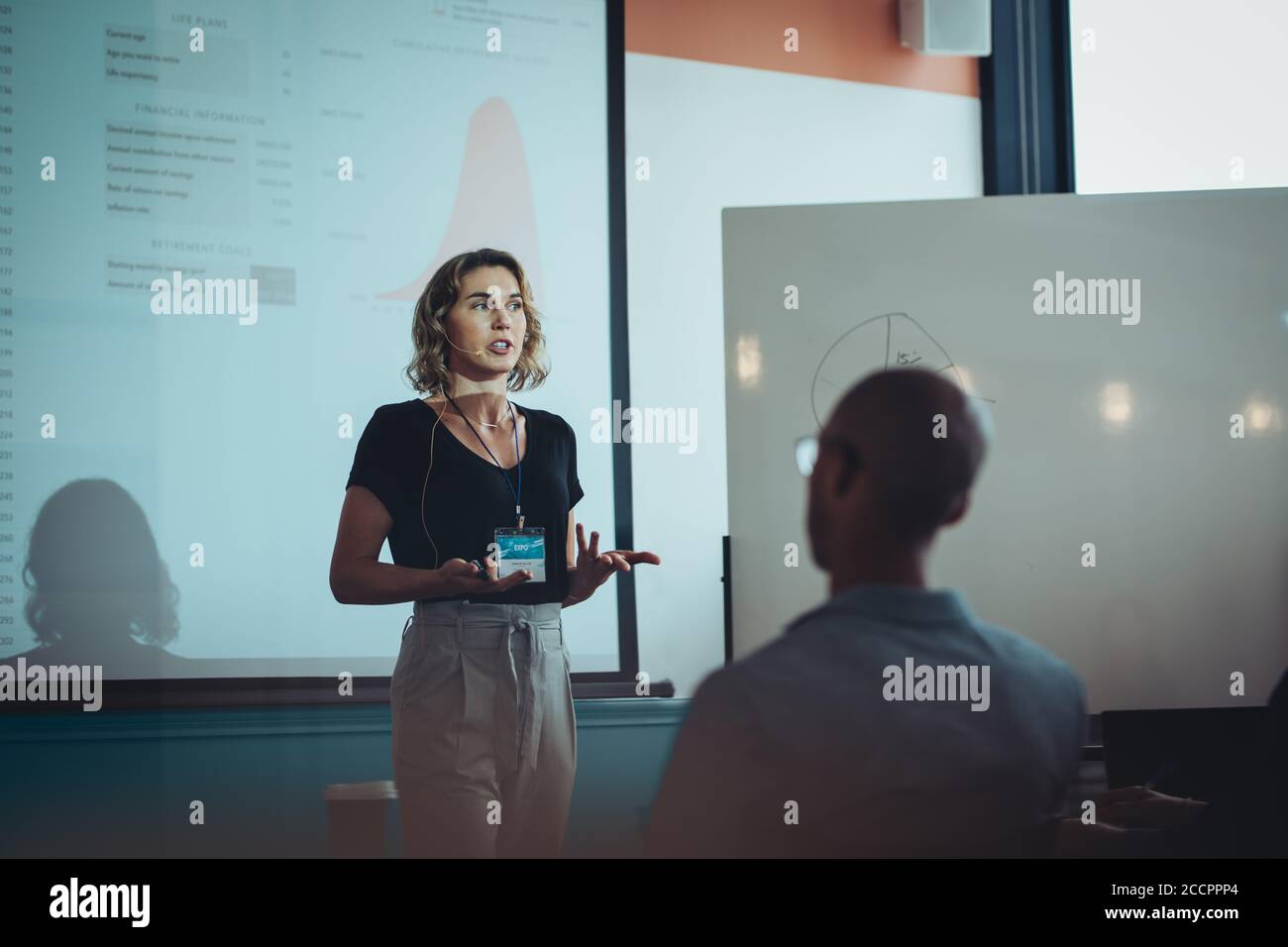 Donna professionista in piedi davanti a uno schermo di proiezione e che presenta le sue idee ai colleghi in una riunione. donna d'affari che sta rispondendo a un seminario. Foto Stock