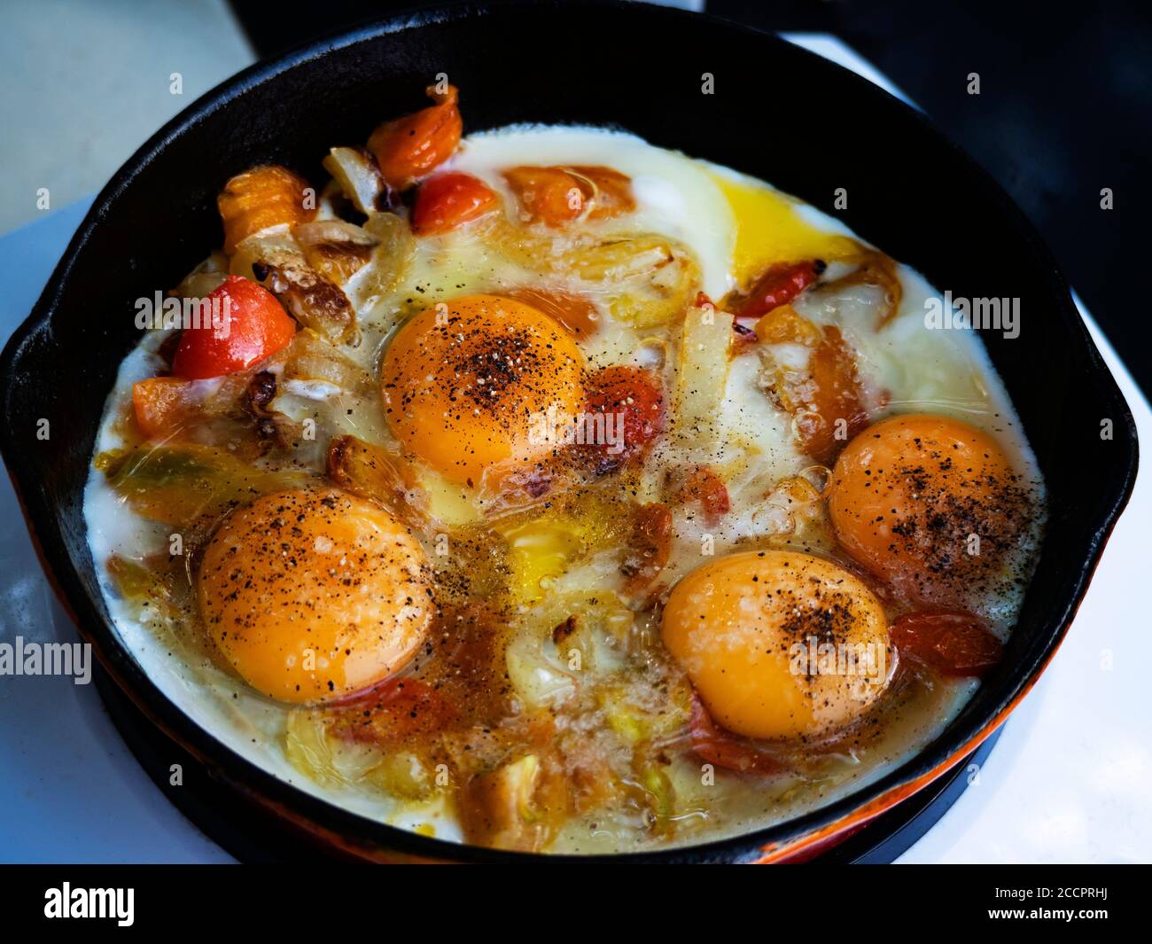Le uova strapazzate con i pomodori vengono fritte in una padella di ghisa su una stufa elettrica di induzione Foto Stock