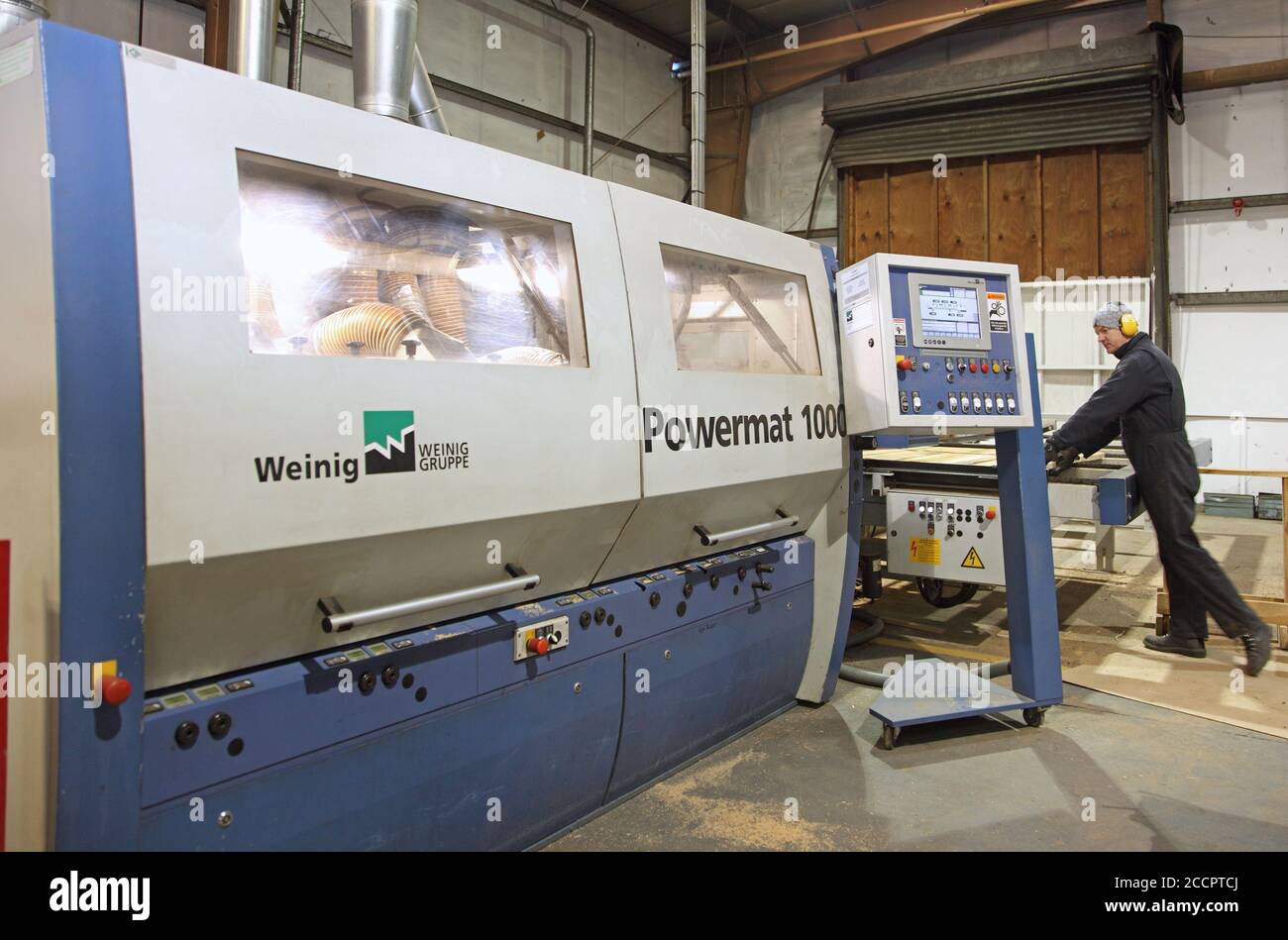 Un lavoratore prepara listelli di legno per una macchina di piallatura e stampaggio controllata da computer in una fabbrica di Falegnameria britannica. Foto Stock