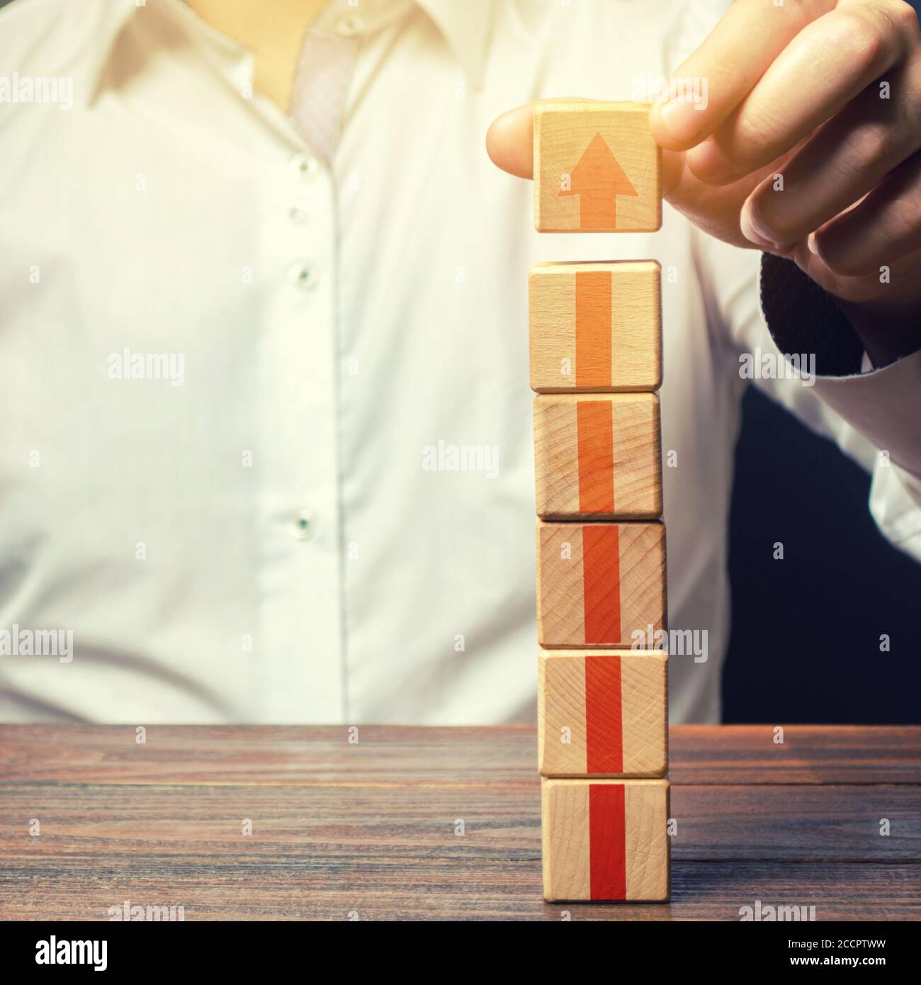 Uomo d'affari costruisce una torre di blocchi con una freccia in su. Promozione della carriera, crescita delle competenze professionali. Crescita dei profitti. Marketing. Migliorare l'efficienza Foto Stock