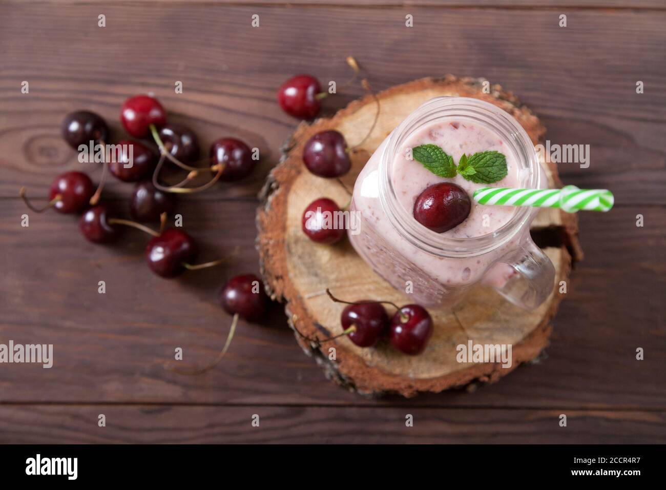 Frullati di ciliegia dolce in un vaso con una paglia, bacche sparse su uno sfondo di legno. Cibo vegetariano. Mangiare sano Foto Stock