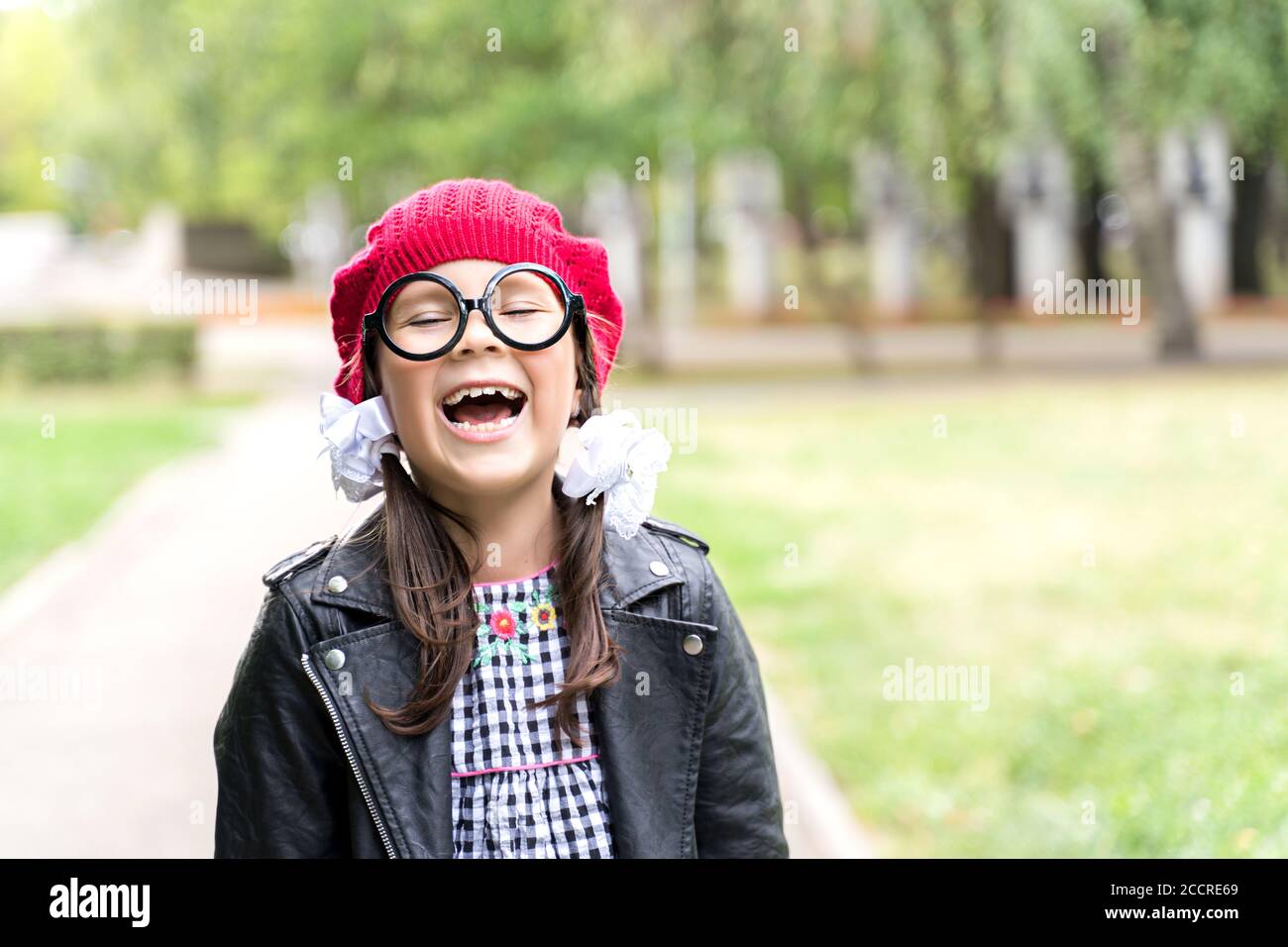 una bambina divertente in un cappello rosso e rotondo gli occhiali ride Foto Stock