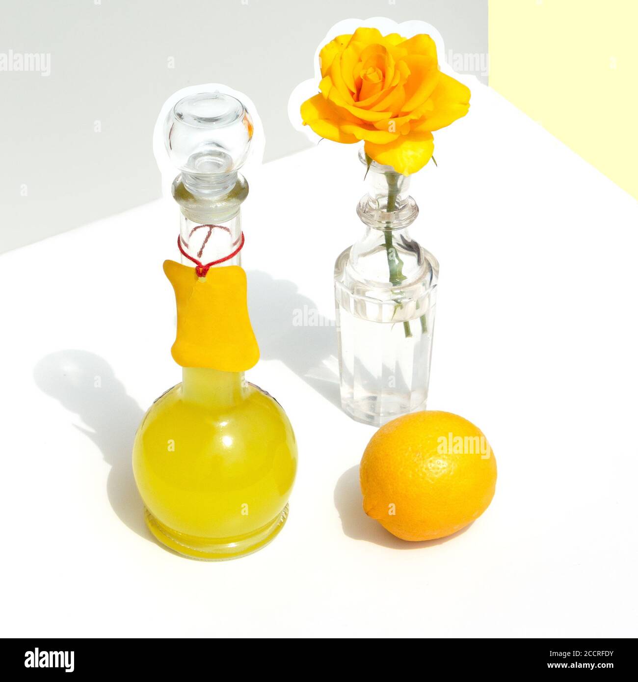 Bottiglia di limoncello italiano, limone e rosa gialla. Moderna vita still minimalistica su sfondo geometrico con luce solare e ombre. Foto Stock